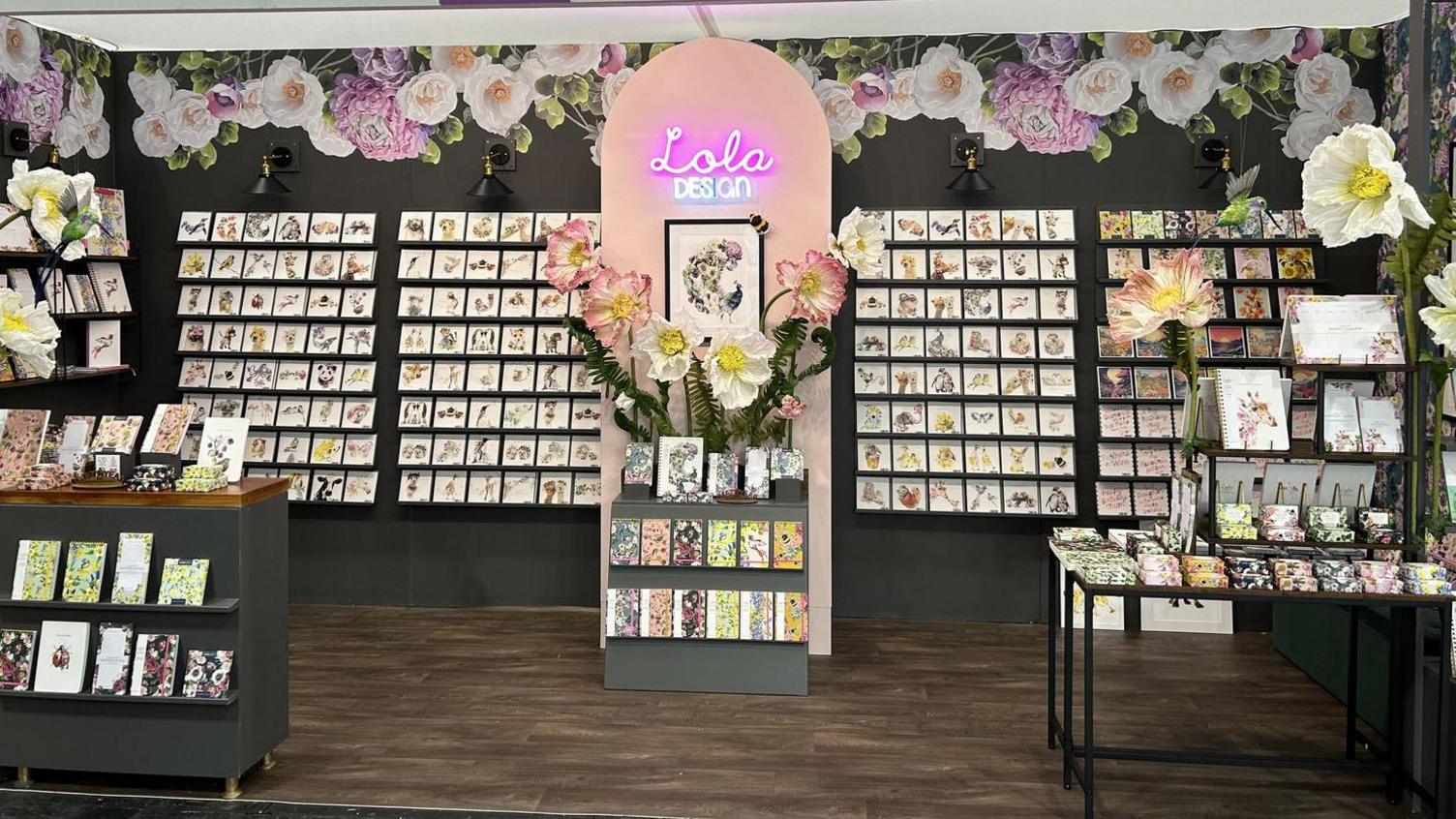 A stand at an exhibition featuring Lola Design's work at an. Many greetings cards are displayed in rows.