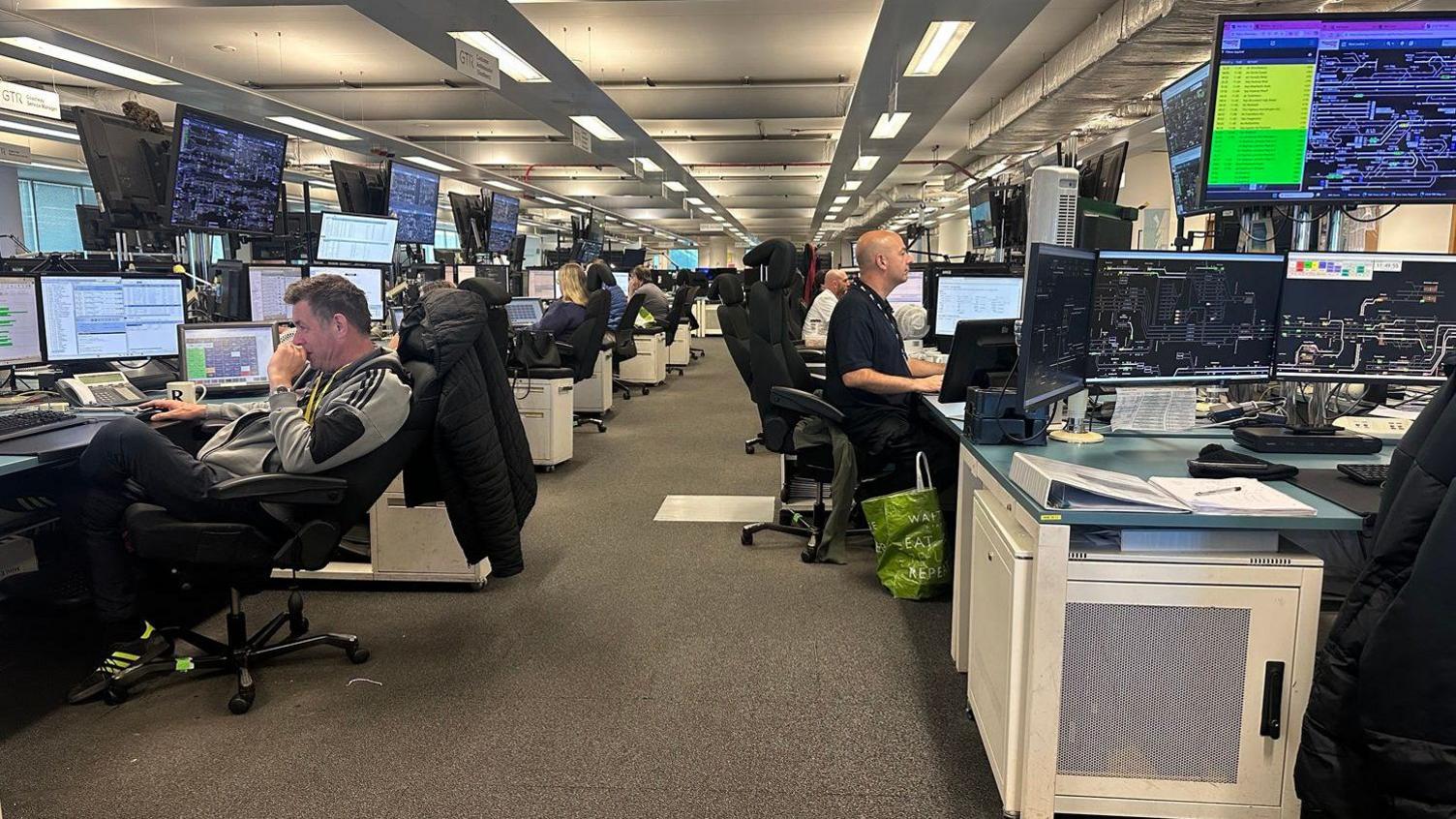 People sitting inside a railway control room. There are a number of people at computers monitoring ongoing incidents.