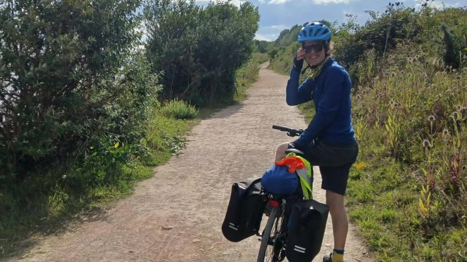 Harry, who wears a blue helmet, smiles while standing over his bike.