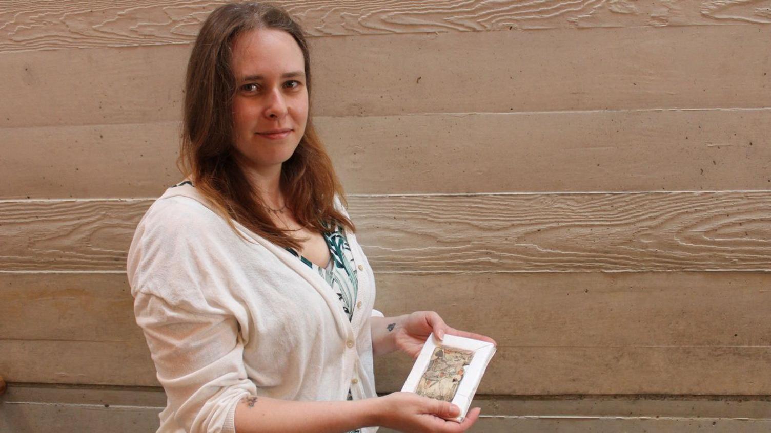 Conservator for the Chatham Historic Dockyard Trust, Alexandra Wade, is holding the Jack of Spades which is secured inside a white frame.