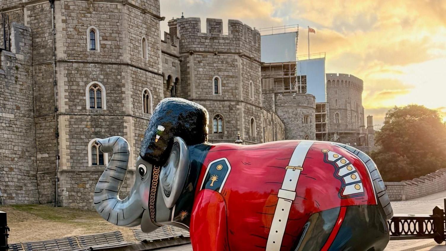 An elephant structure, dressed like a member of the King's Guard, is pictured on a pavement with Windsor Castle in the background.