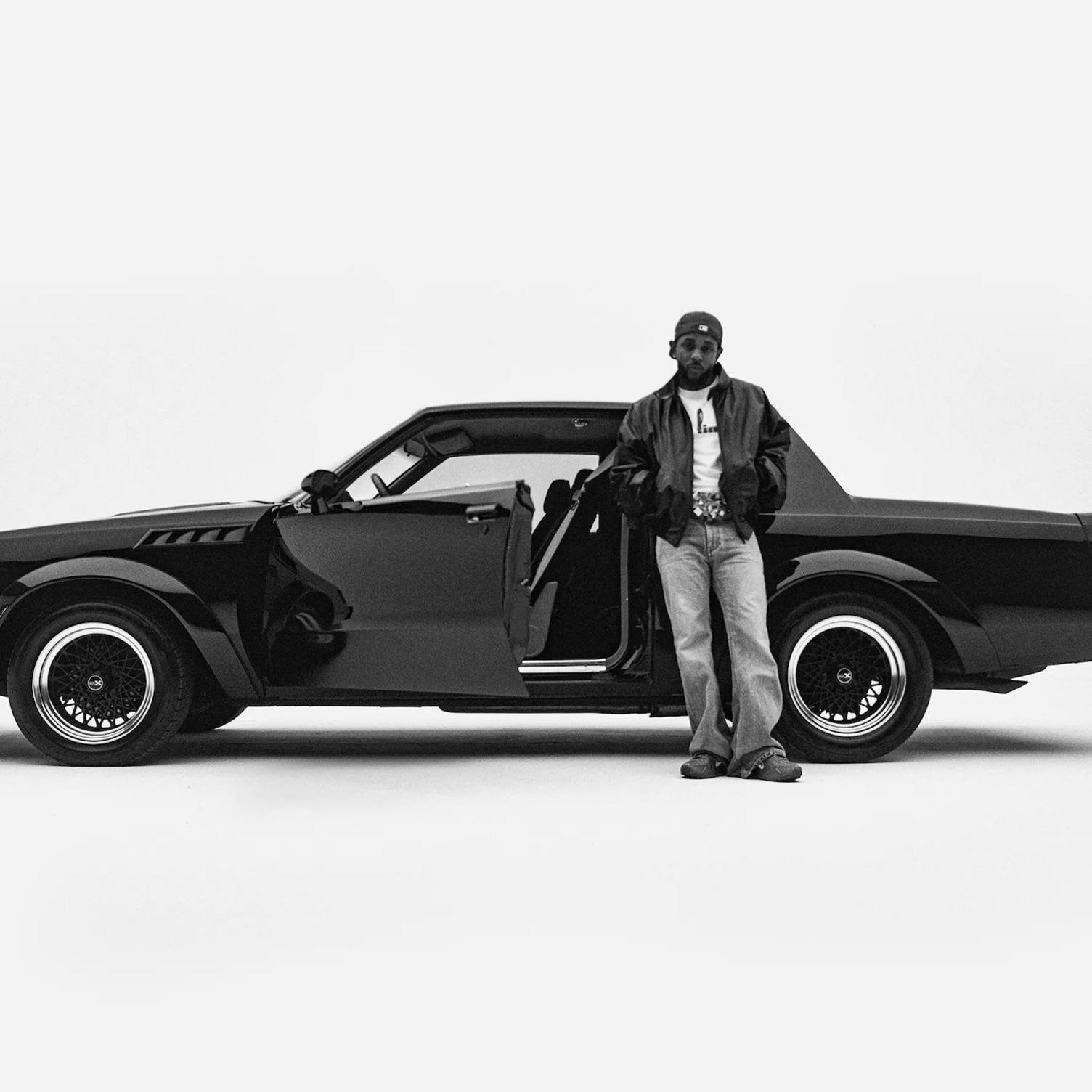 Artwork for Kendrick Lamar's album, GNX. A black and white image of a two door sports car and Kendrick Lamar - wearing a leather jacket and jeans and a baseball cap. The image looks like it was taken in a photographic studio as the background is entirely white.