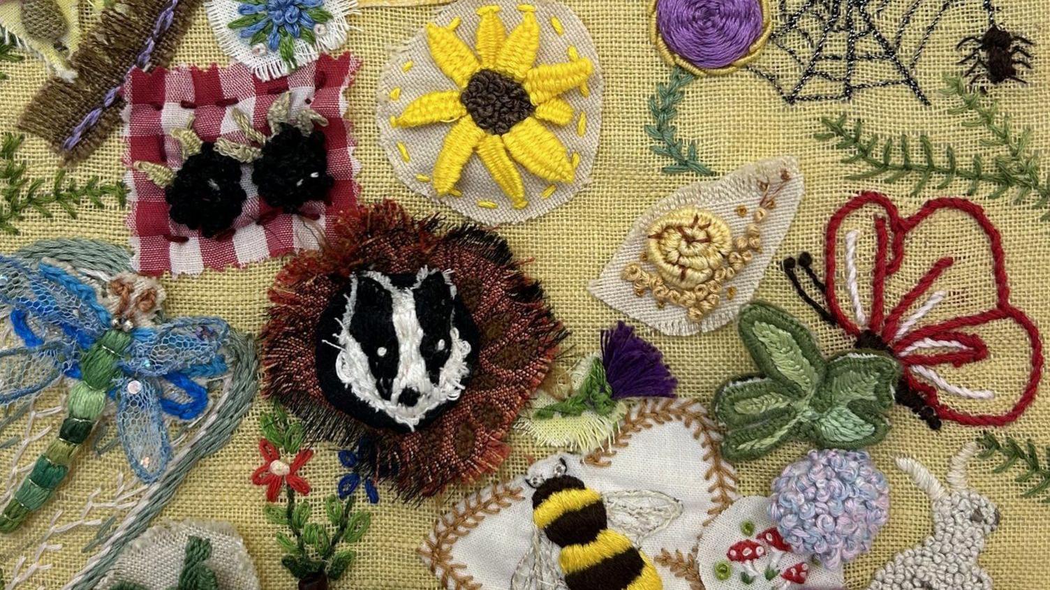 A close-up of some of the embroidery, which includes a black and white badger on a brown background, a yellow sunflower and a black and yellow bee with white wings and brown-ish stitching around it.