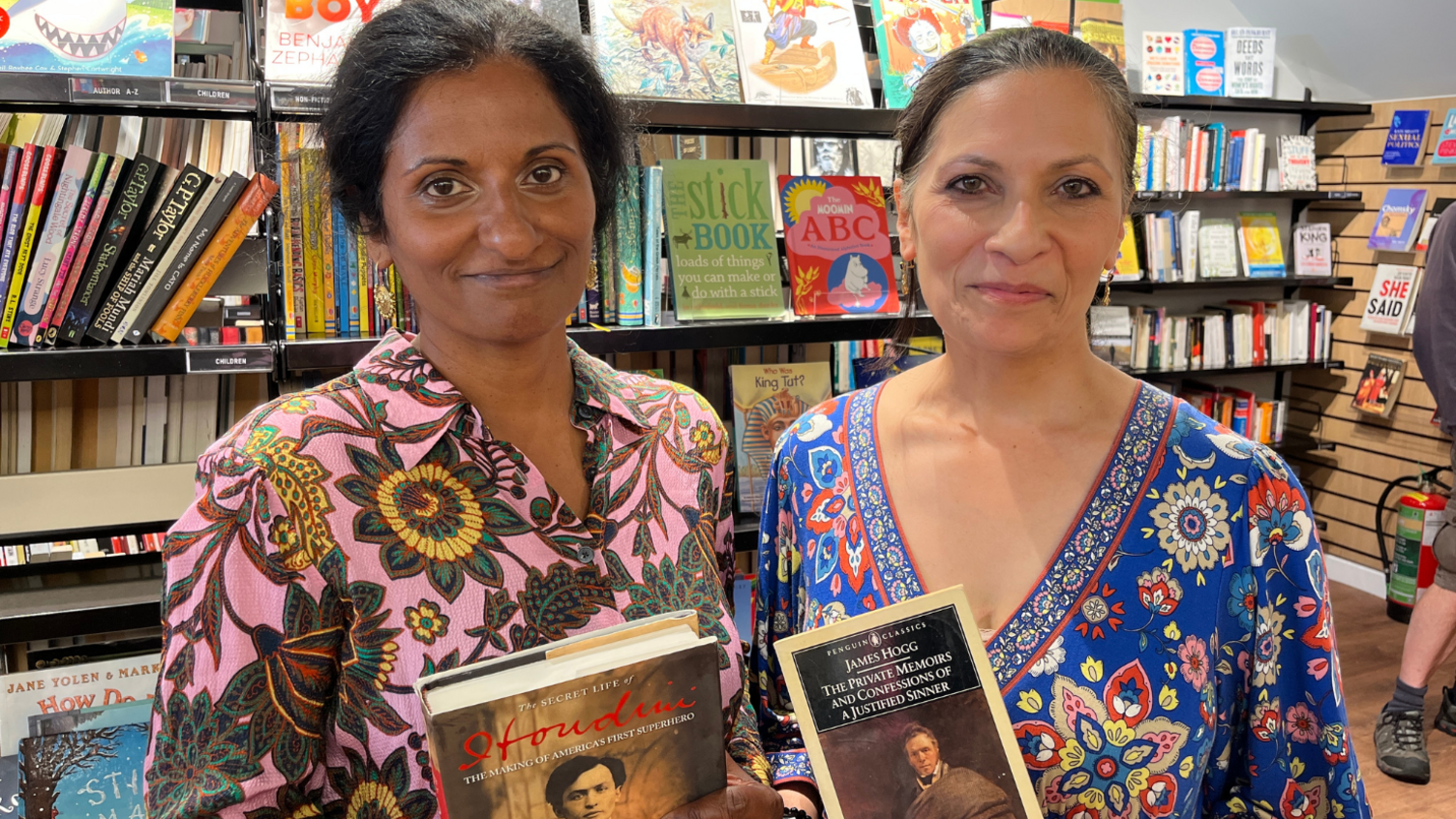 Sisters Seeta and Lizzie Seetharaman pictured with their books at the Oxfam bookshop in Hove, East Sussex. Seeta bought a biography of Houdini while Lizzie bought The Private Memoirs and Confessions of a Justified Sinner. Seeta is wearing a pink and green floral dress, while Lizzie is wearing a blue, red and yellow dress.