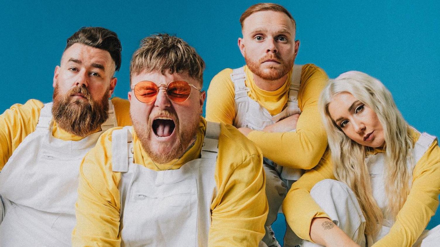 The indie-pop band Lottery Winners wear white boiler suits over yellow tops, and pose against a pale blue background. Lead singer Thom Rylance is positioned at the front, and screams at the camera