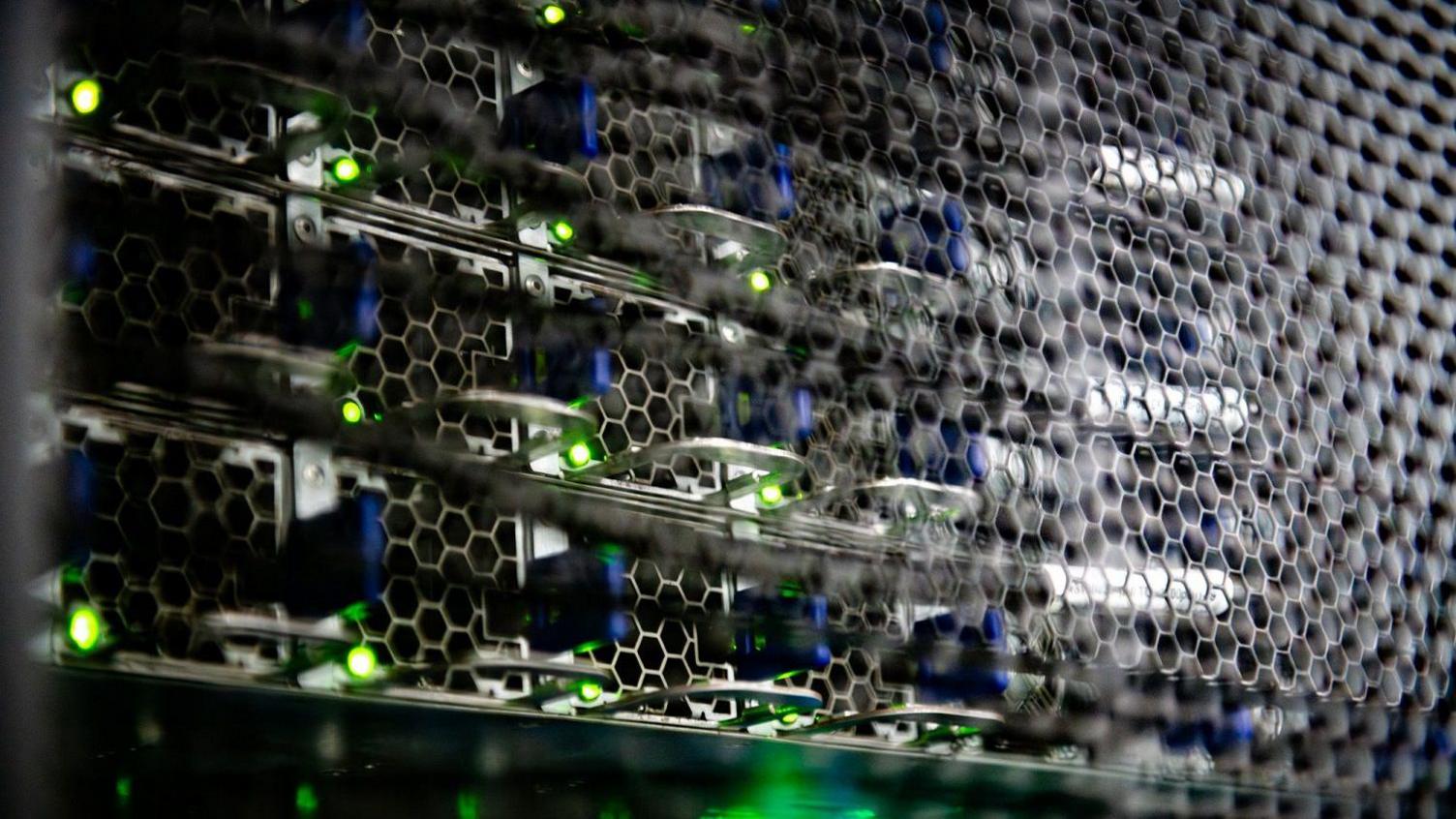 Another part of the computer, seen through a metal hexagon grill. There are blue and green lights across the unit in a repeated pattern. 