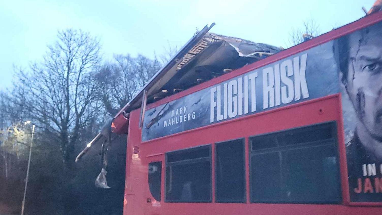 A red bus in a road with its roof peeled backwards.