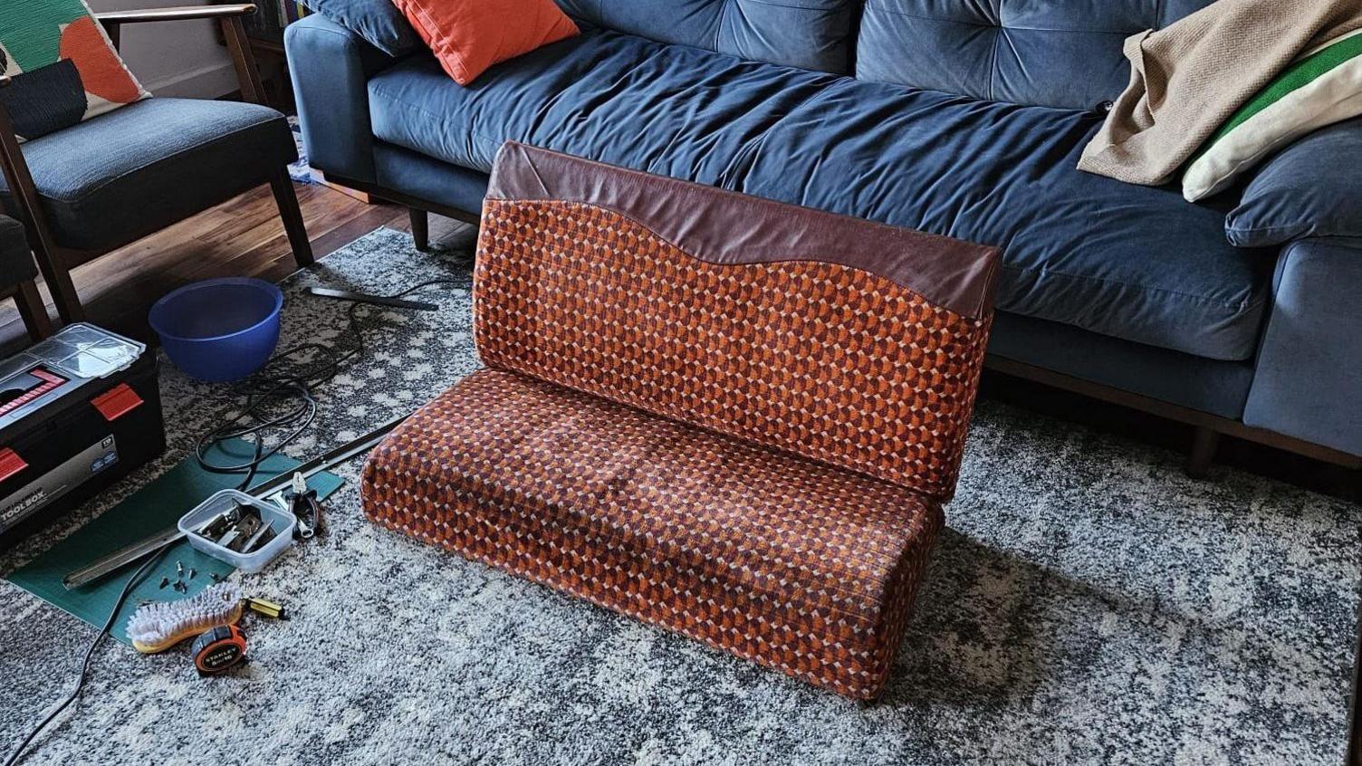 A bright orange and red subway seat converted into a couch without armrests and legs in a living room.