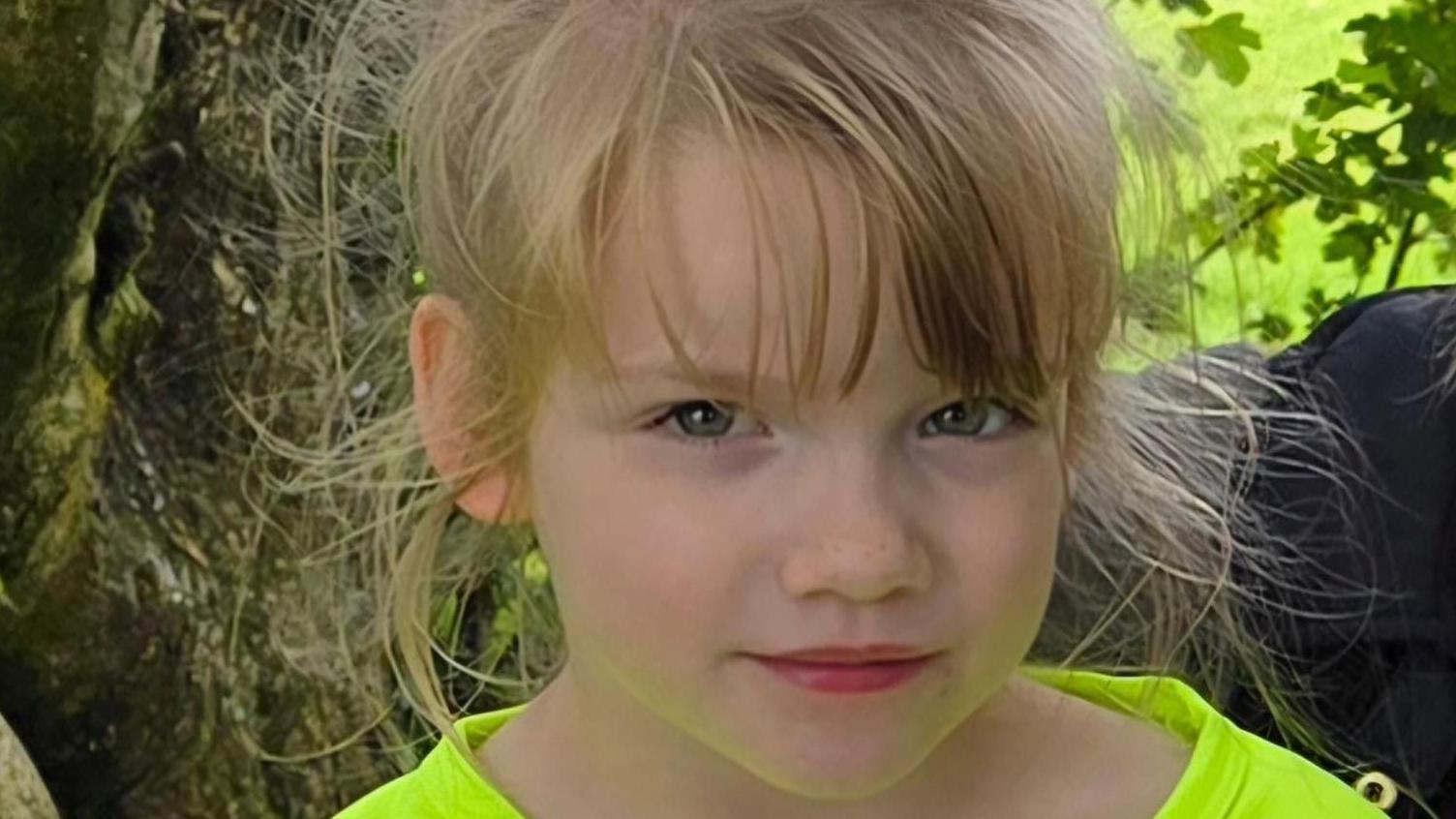 Hope looking directly at the camera. She is wearing a luminous green t shirt. She has blonde hair and blue eyes.