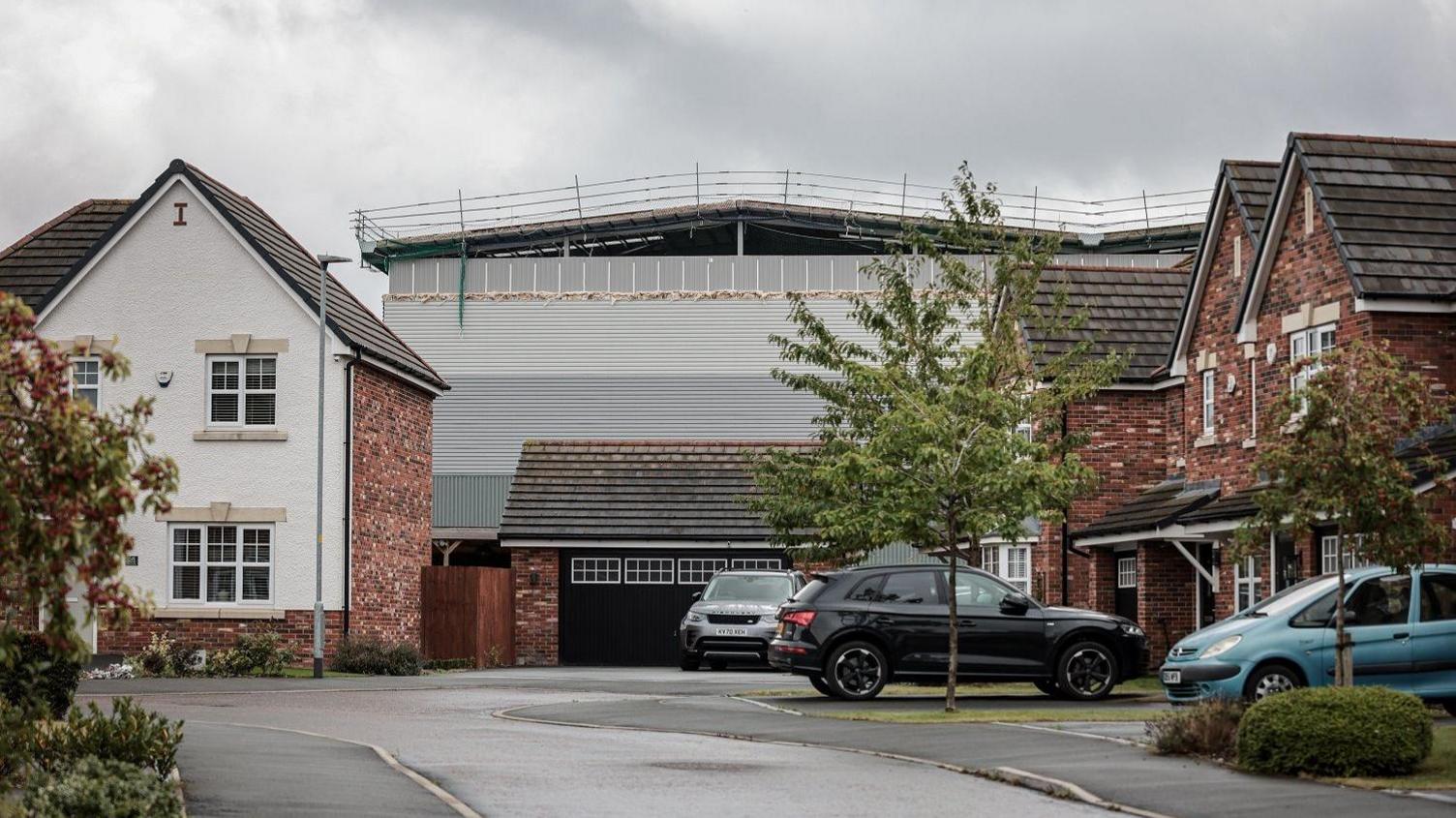A semi-constructed giant steel-framed warehouse looms behind brick houses.