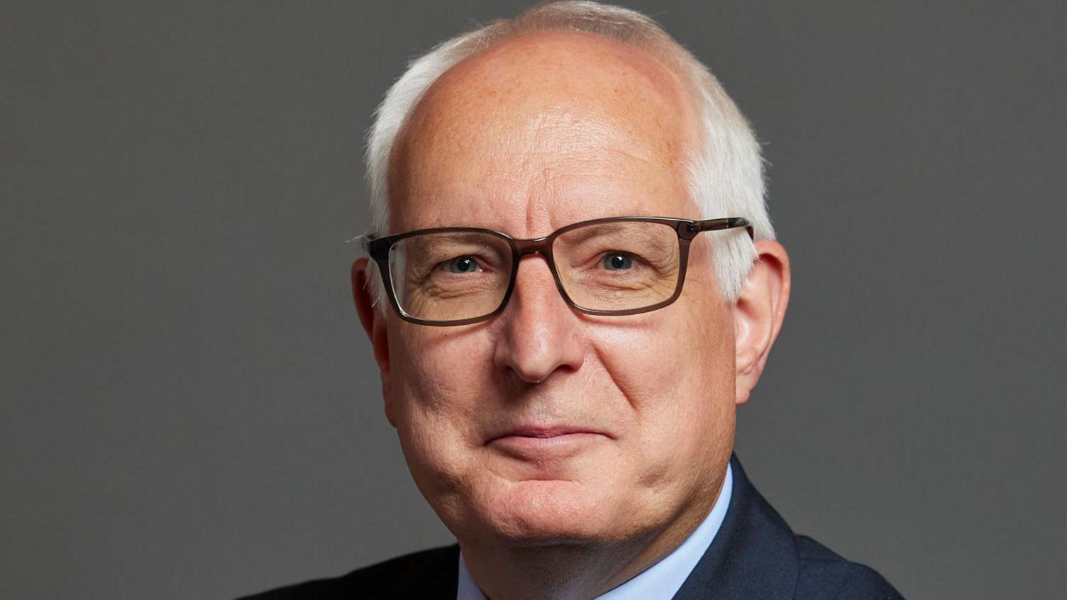 Official parliamentary photo of Neil Duncan-Jordan. He is wearing a suit and dark-rimmed glasses. He has white hair and is smiling