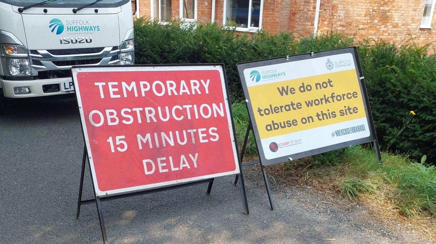 Suffolk Highways work signs reading "TEMPORARY OBSTRUCTION 15 MINUTES DELAY" and " We do not tolerate workforce abuse on this site"