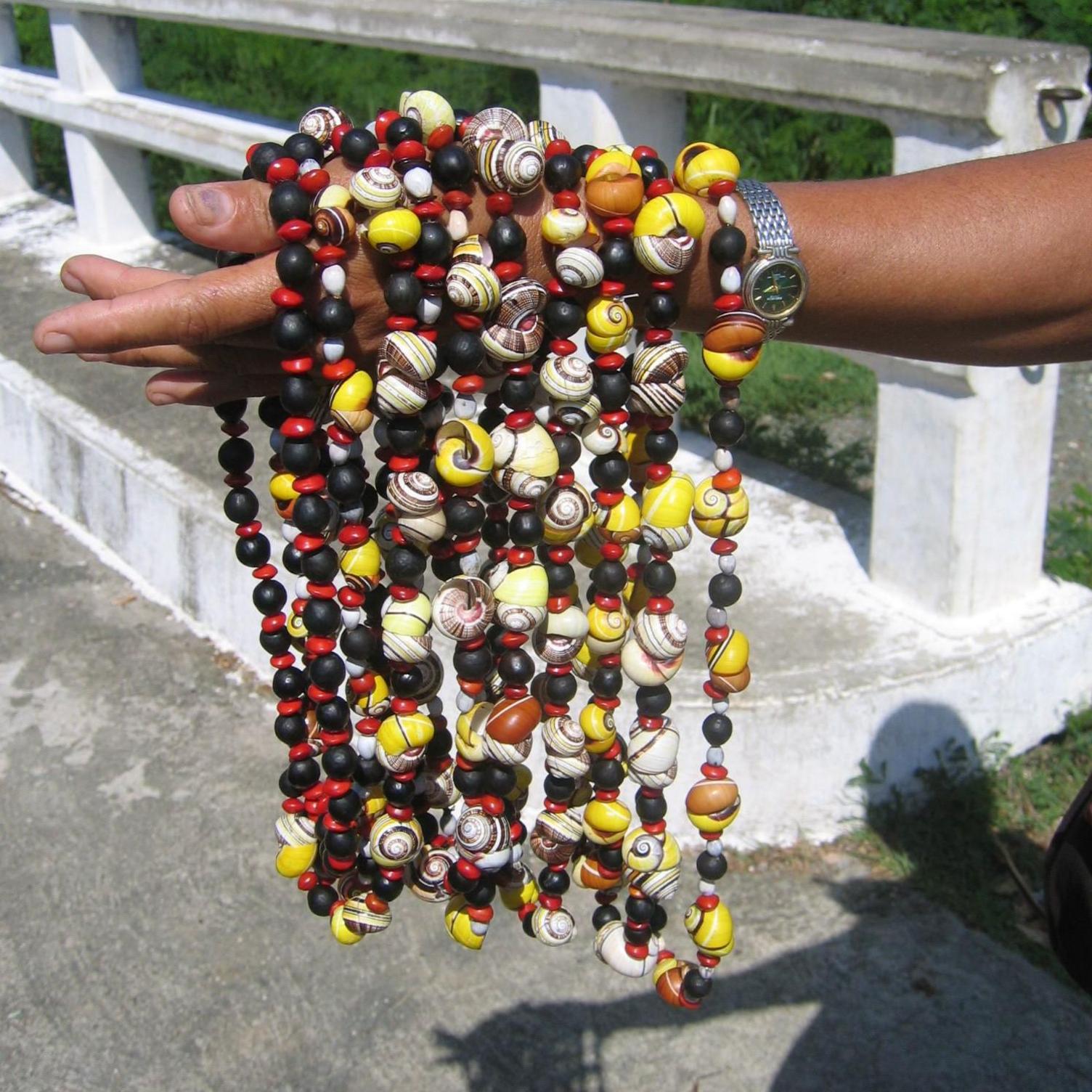 The arm of a person held out with about 10 colourful, beaded necklaces draped over it. When you look more closely, some of these beads are actually colourful snail shells. Some of these are endangered Polymita snail shells .