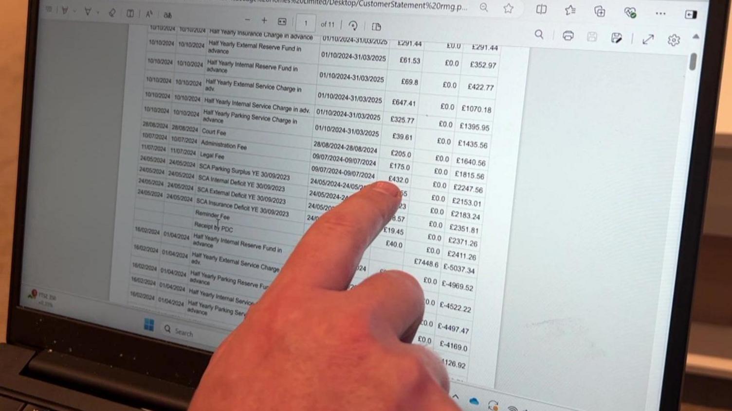 A laptop screen showing Joe's statement from RMG and his finger pointing at legal fees. 