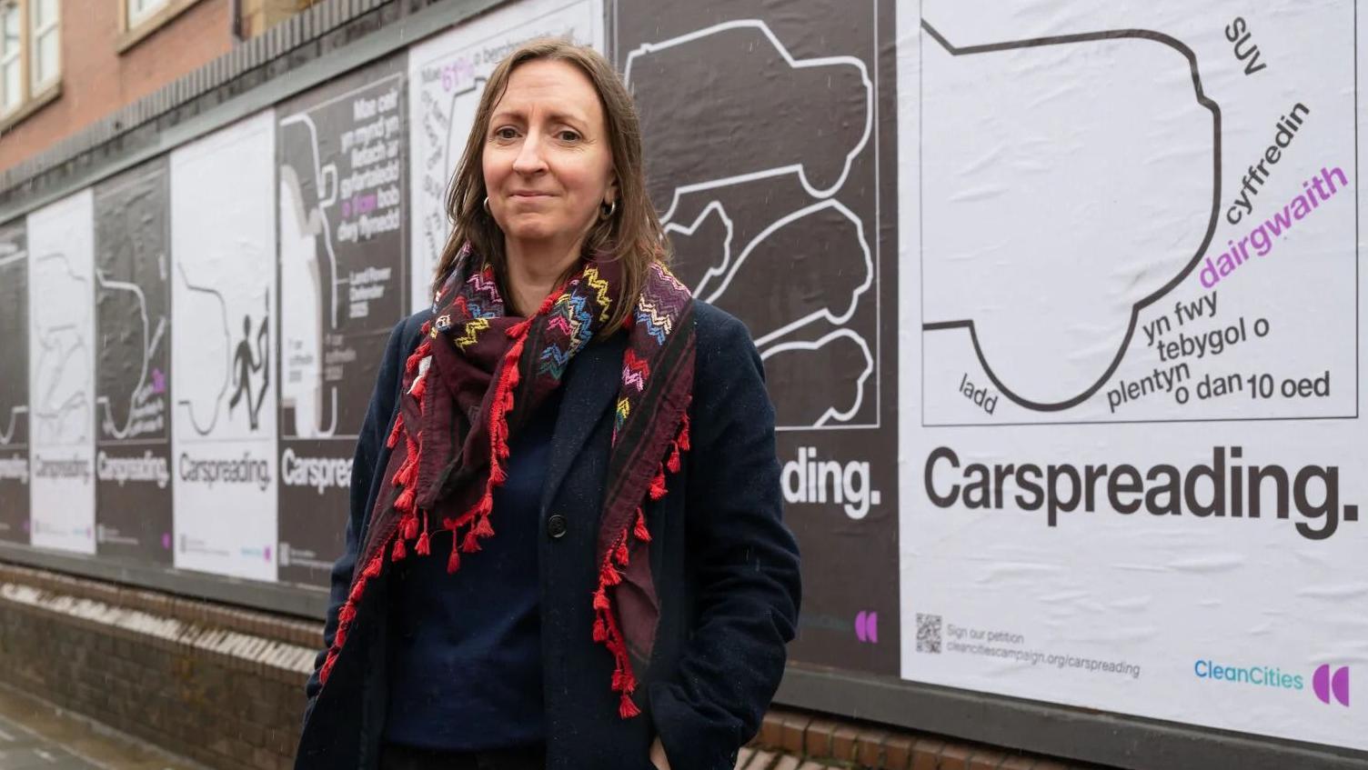 Helen Edwards stands in front of a Clean Cities campaign poster highlighting 'carspreading' or the growing size of vehicle
