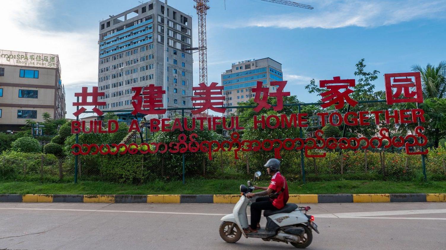 A man riding past a red sign saying 'Let's build a beautiful home together'  