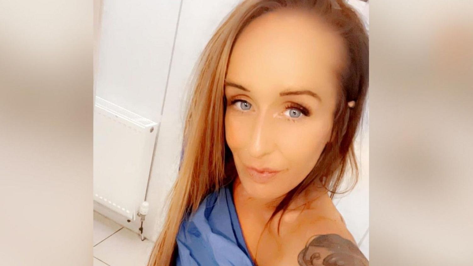 A woman takes a selfie - she has long straight strawberry blonde hair and a powder blue dress which is off the shoulder.
