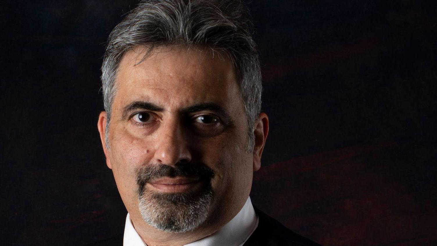 Antony Antoniou with dark hair and beard against a dark background