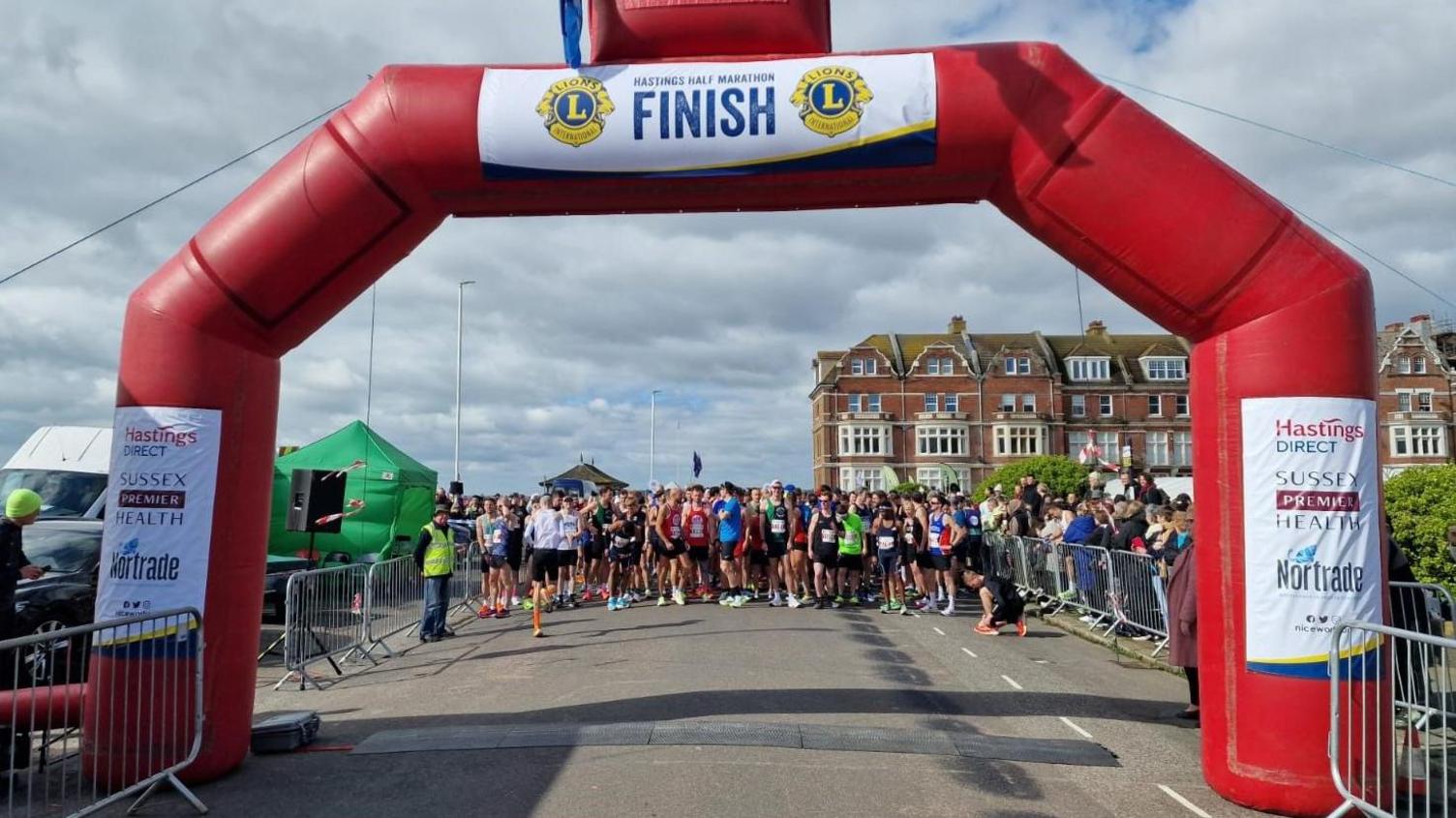 Many runners in bright coloured running clothes line up behind an inflatable red archway on Sea Road in Hastings for the 40th half-marathon 