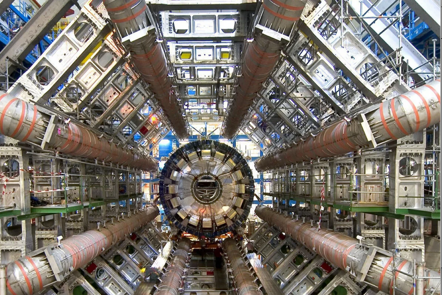 A huge circular “engine” sits at the tunnel’s centre, surrounded by criss-crossing metal beams, pipes and cables, forming a vast, brightly lit, cathedral‑like space of shimmering steel.