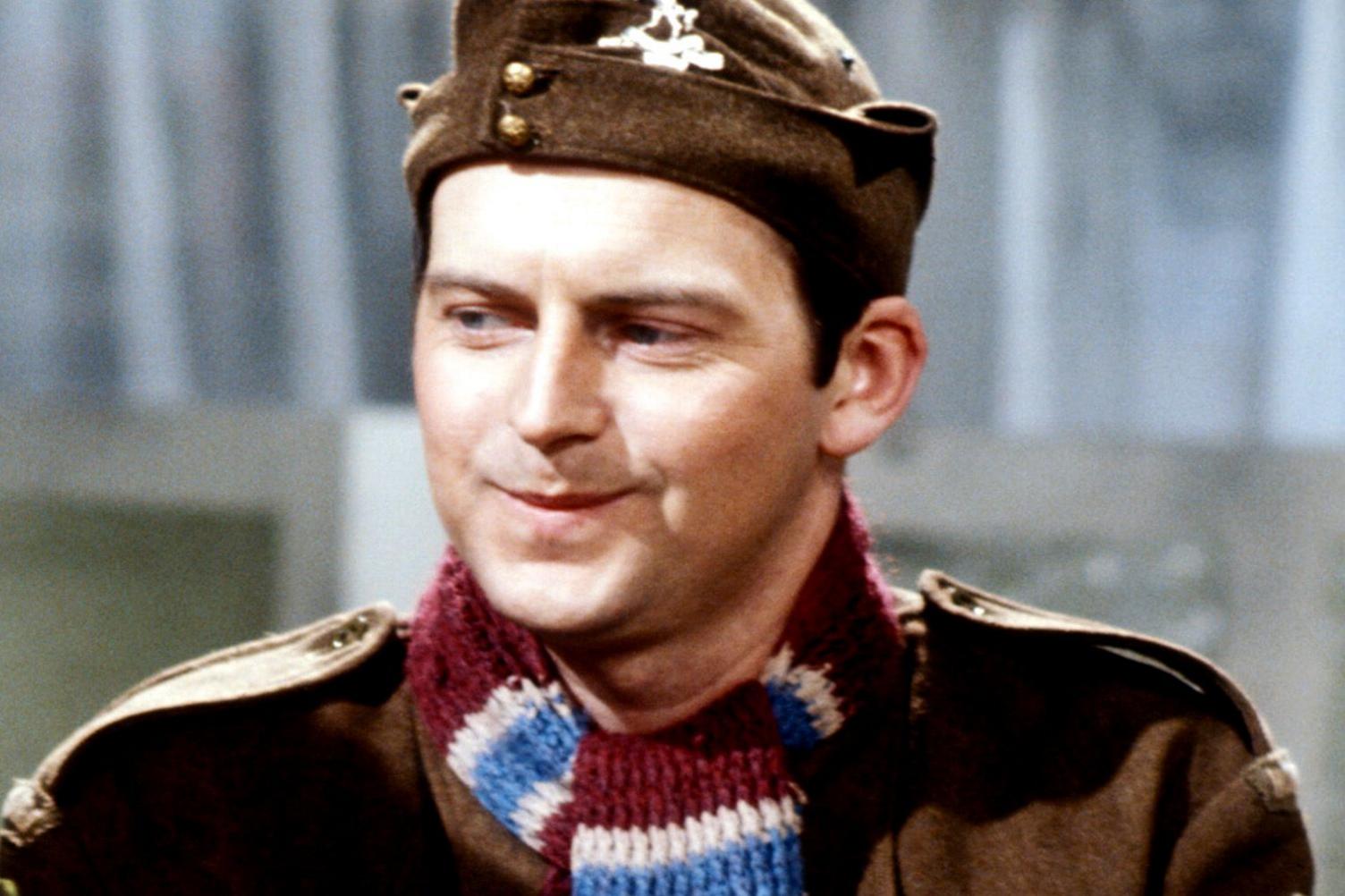 A still from Dad's Army shows a young Ian Lavender playing Private Pike. He smiles shyly dressed in his uniform and a red and blue scarf.