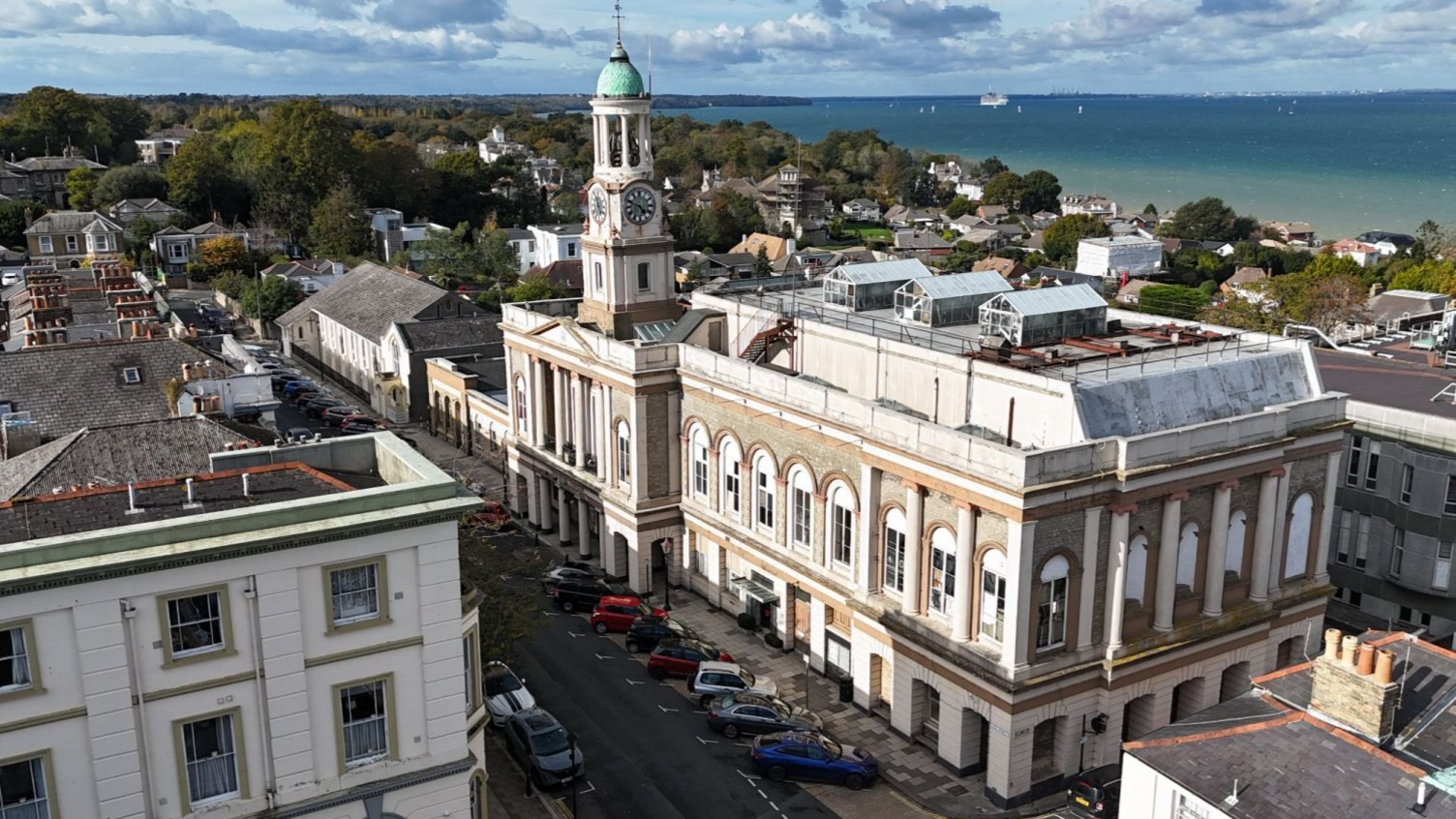 A large picture of the Ryde Theatre, with a clock tower in the front and centre of the building. The Solent can be seen a short way behind the theatre.