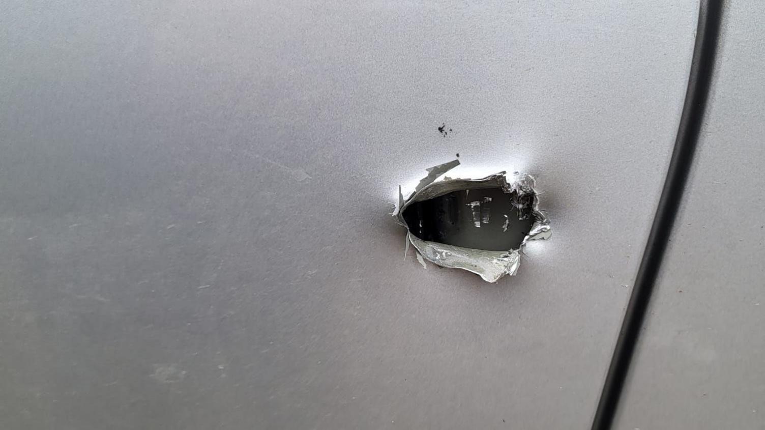 A smooth silver van surface with a vicious hole cut