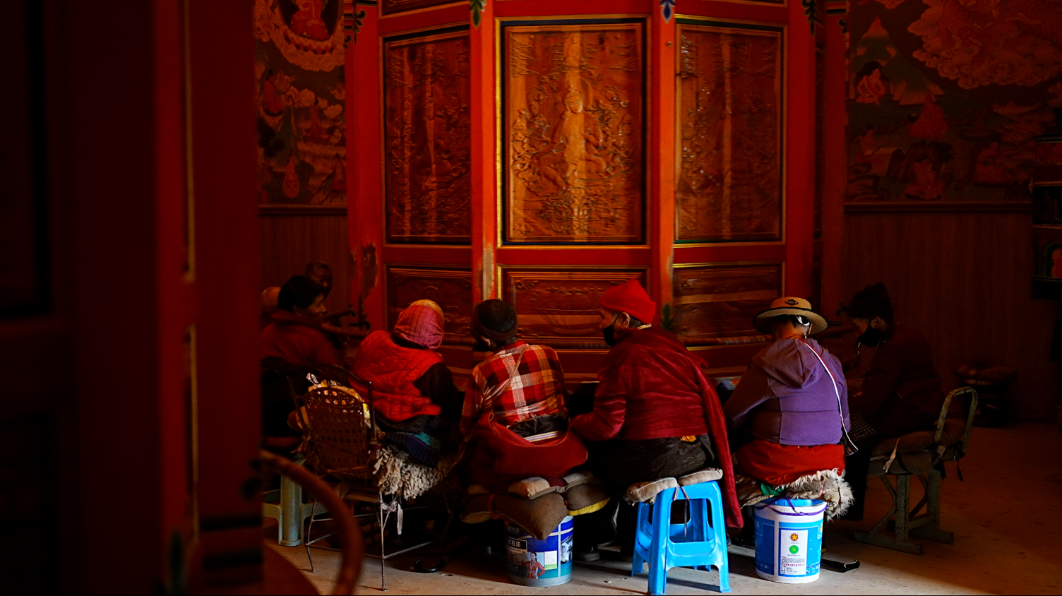 Tibetan women sit by a prayer wheel inside a monastery