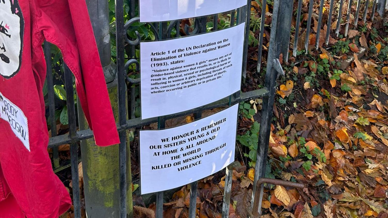 Laminated statements printed on white card as part of the Raising the Red project. They have black text on them, explaining that the exhibit aims to raise awareness of violence against women and girls. 