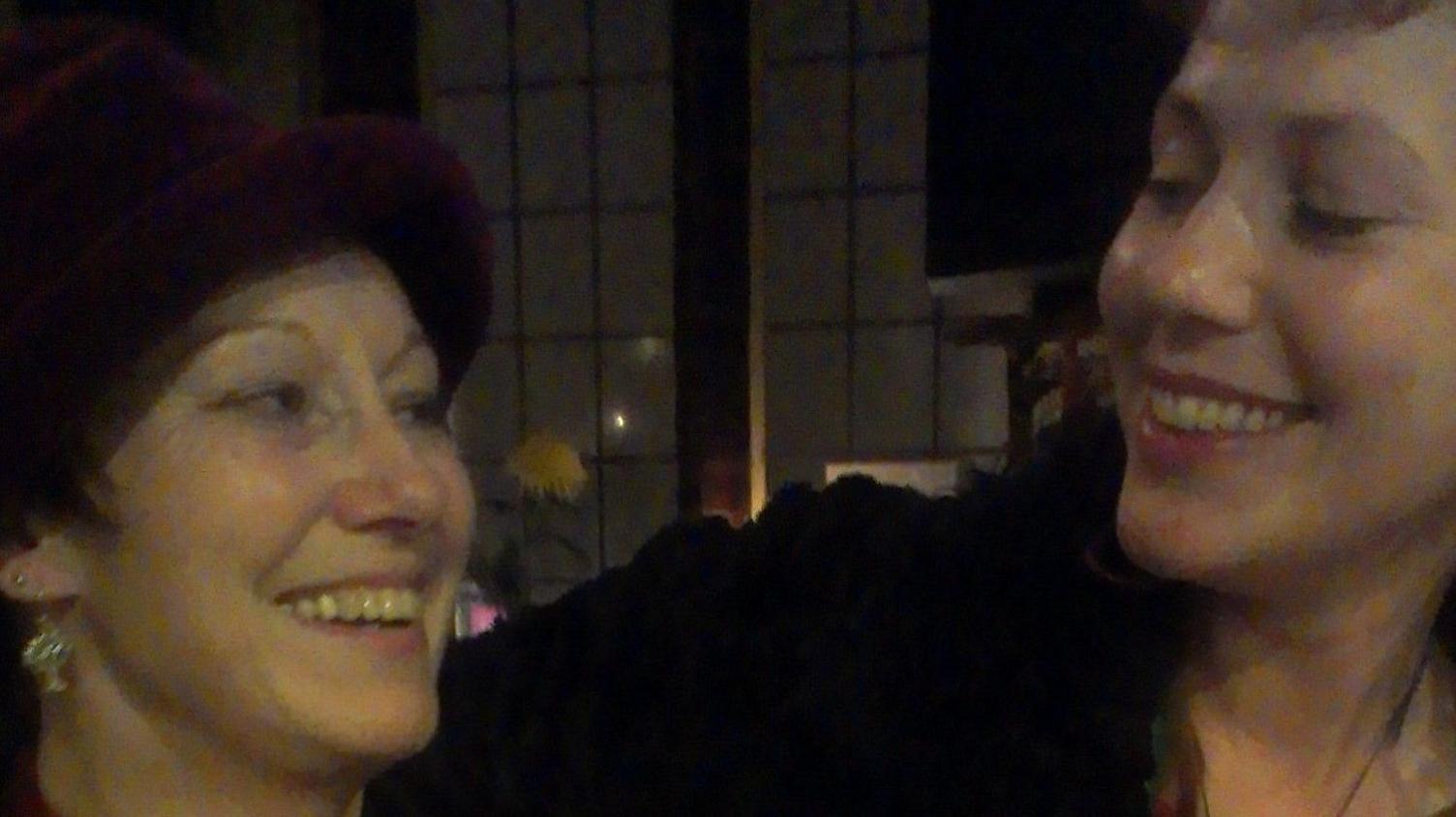 Kat and their mum in a bar. They are smiling at one another.