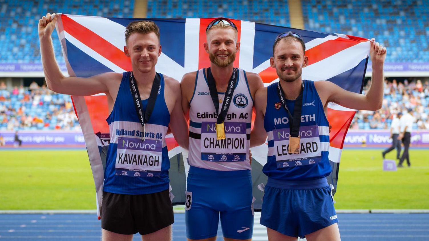 Jack Kavanagh with a GB flag on the medal podium at the UK Athletics Championships in a stadium in Birmingham. 