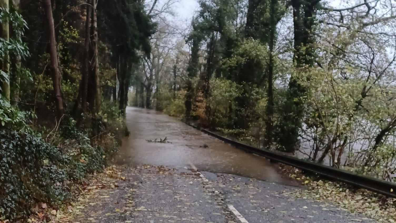 Photo of a flooded road with water covering the road entirely with the river to the right.