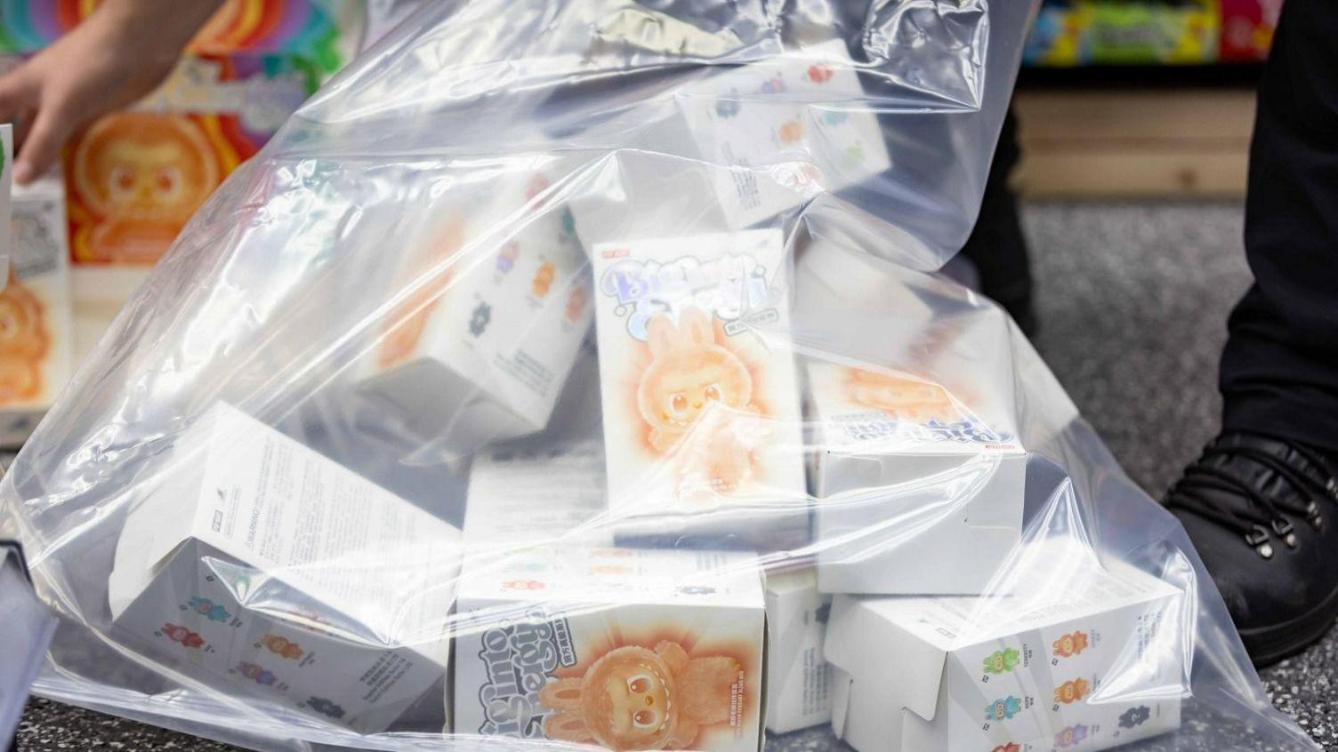A large clear plastic bag containing around a dozen white boxes with a picture of a furry monster creature.