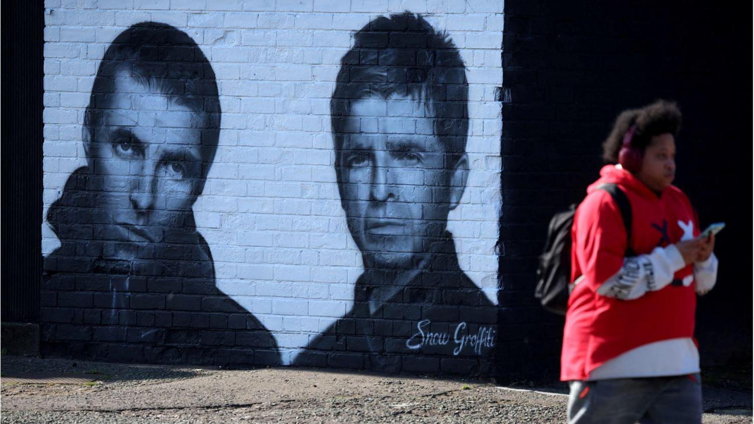 A man walks past a mural of Oasis band members Liam and Noel Gallagher by artist Snow Graffiti on the wall of the Coach and Horses pub in Whitefield, near Manchester.