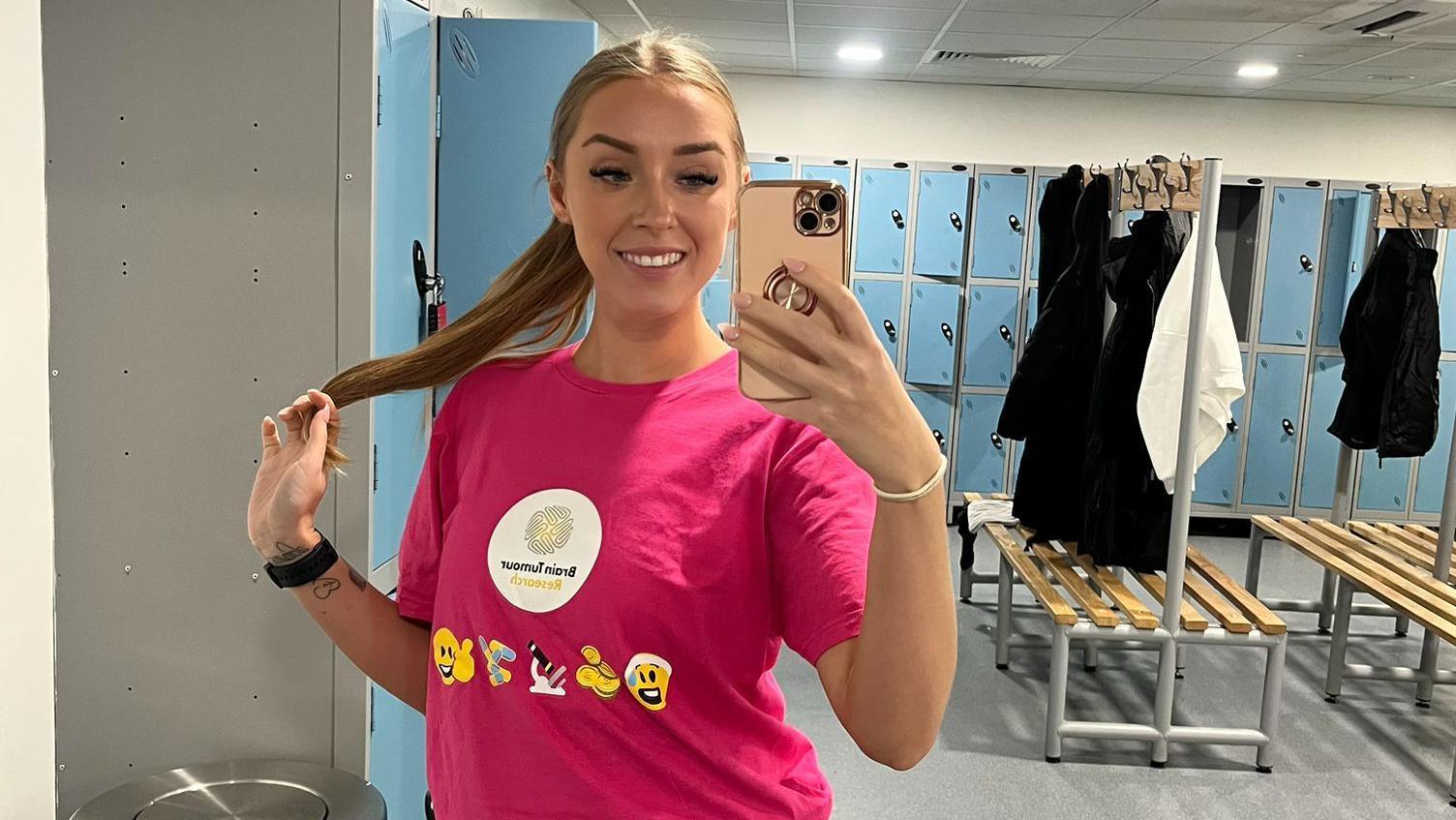 Ms Papadopoulos Green in a bright pink t-shirt which reads 'Brain Tumour Research', she is taking a mirror selfie and is in a changing room. 