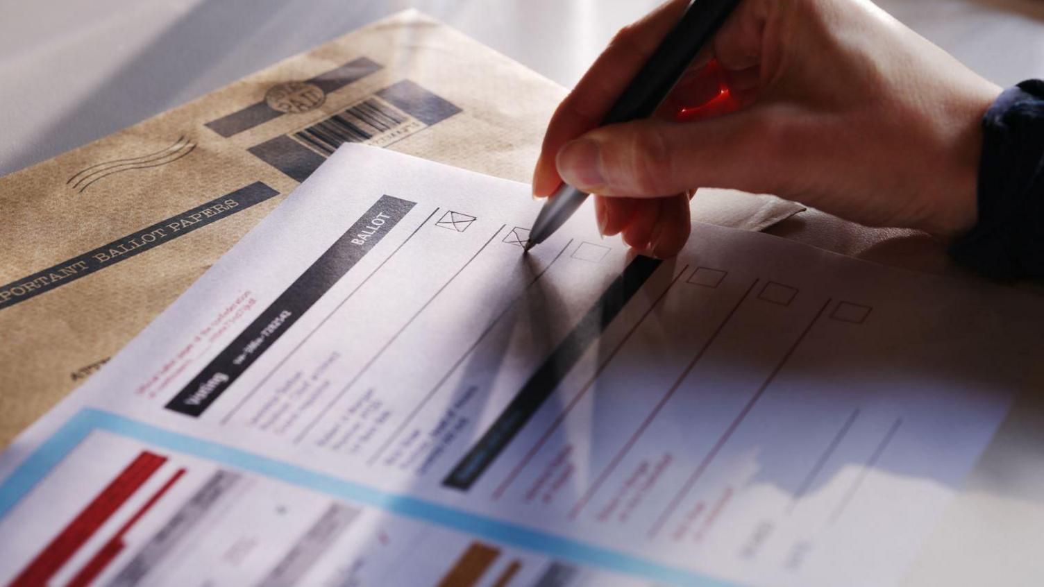 A hand in shadow holding a pen over a piece of paper with blurred words on it