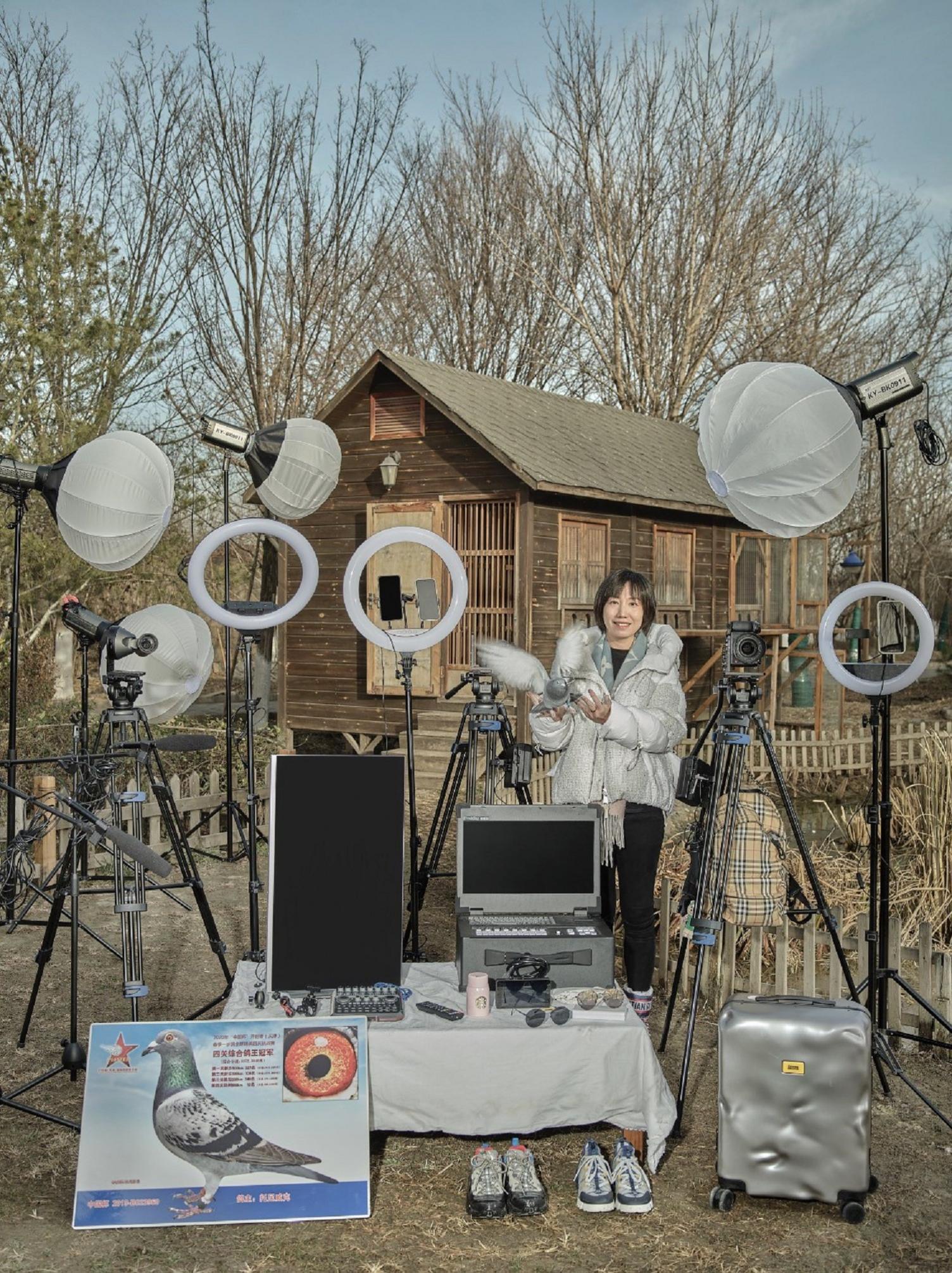 Woman holds a carrier pigeon in her hand while surrounded with professional lighting and camera equipment.