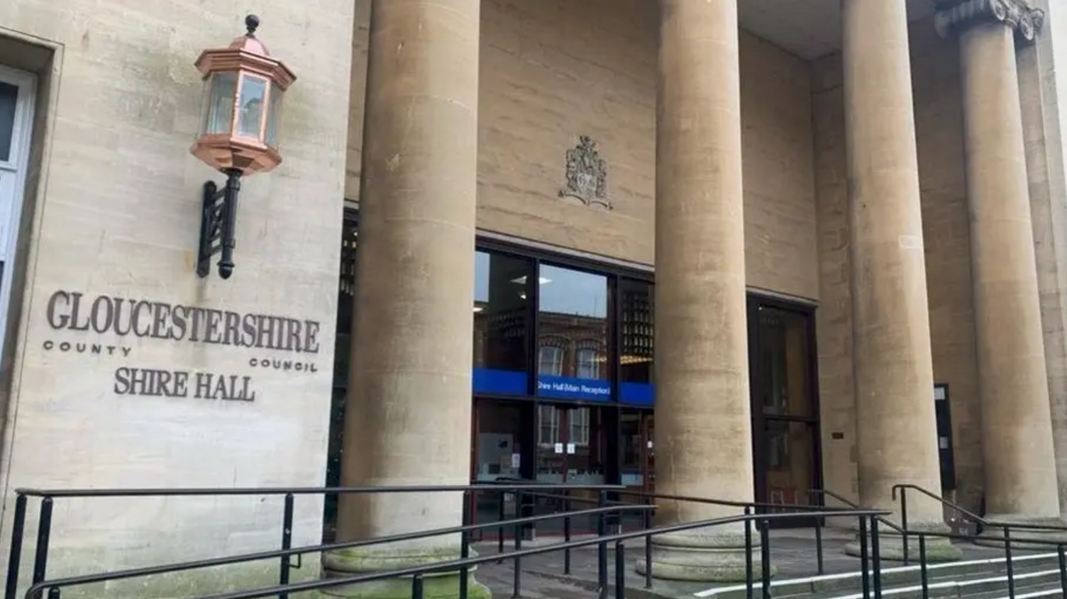 The entrance to Shire Hall. There are four large pillars in front of the glass entrance doors. To the left is a copper street lamp.