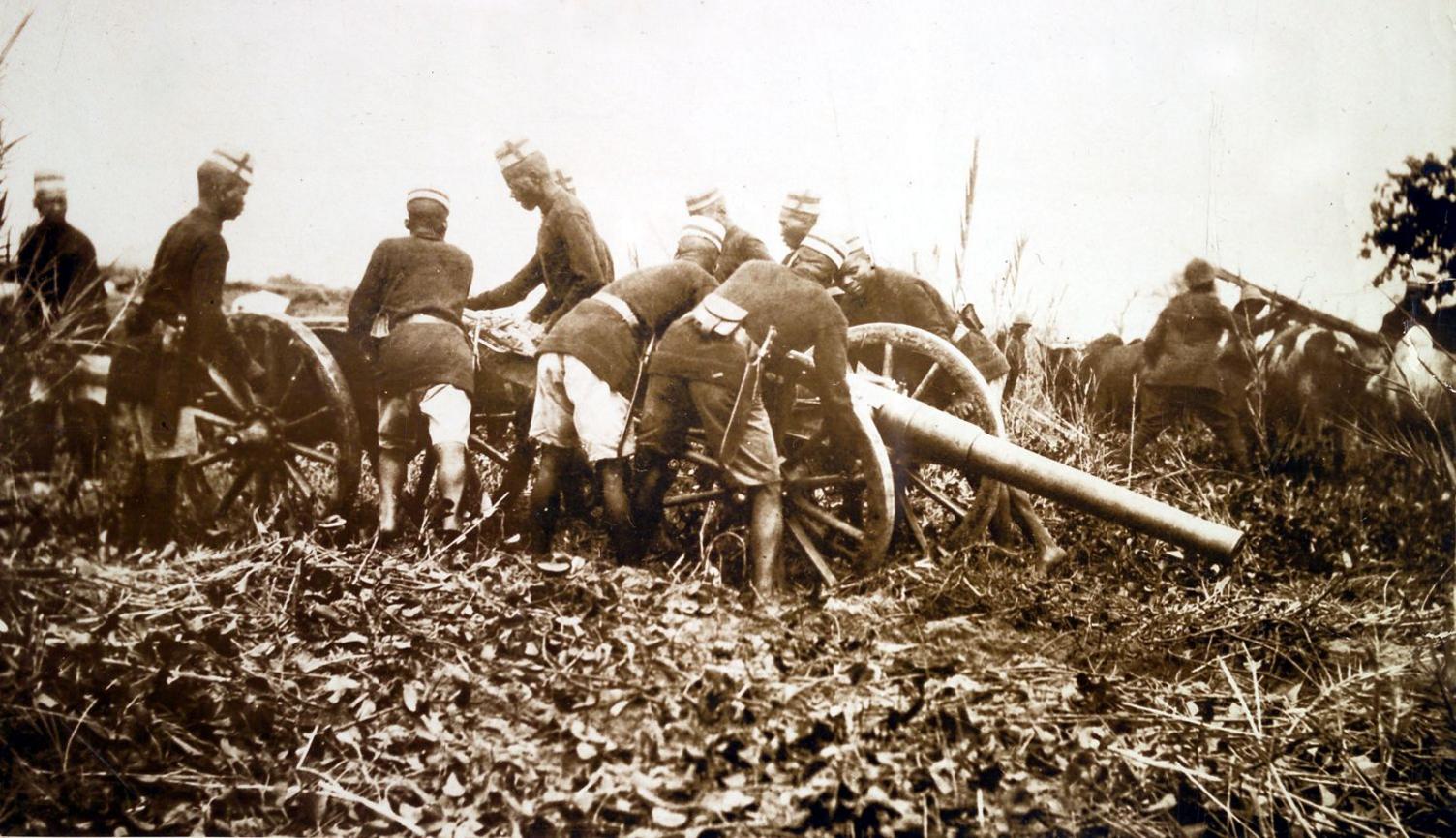 A sepia-toned photo shows men in military gear handling a cannon.