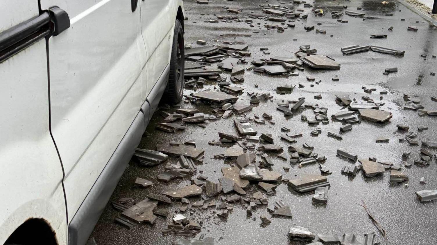 Roof debris is seen all over the floor next to a white van.