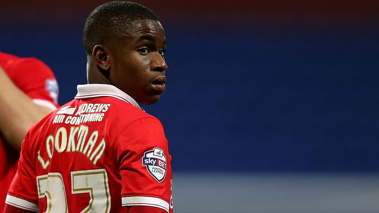 Ademola Lookman, seen from behind wearing a red shirt with white trim, looks over his right shoulder during a football match