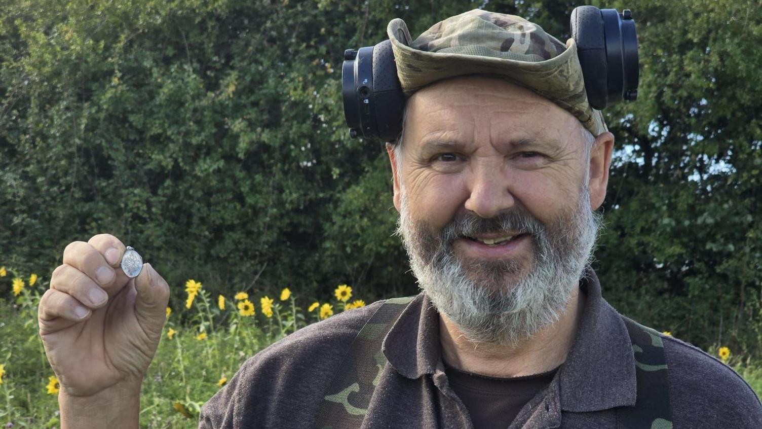 Mark, a metal detectorist, in his gear, holding up the silver locket and smiling