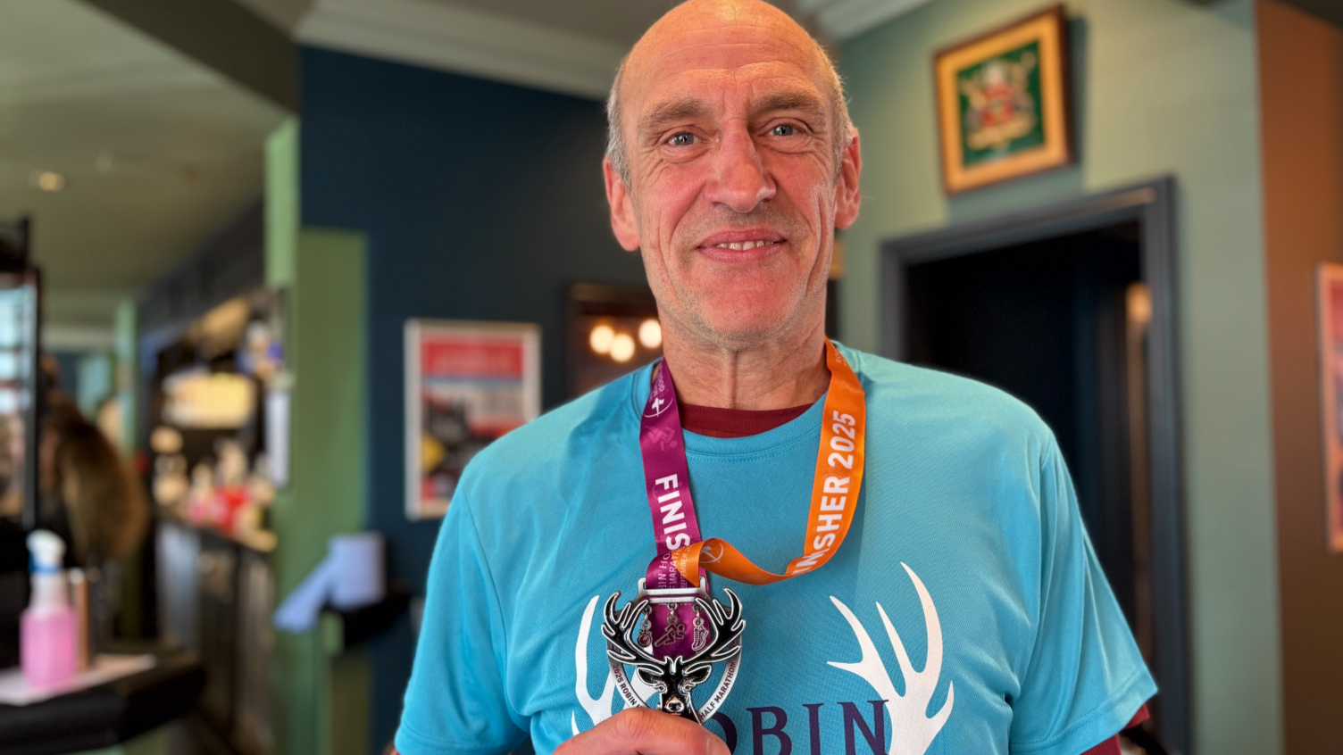 Kevin Walker looking at the camera wearing a blue Robin Hood Half Marathon t-shirt and holding his finishing medal.