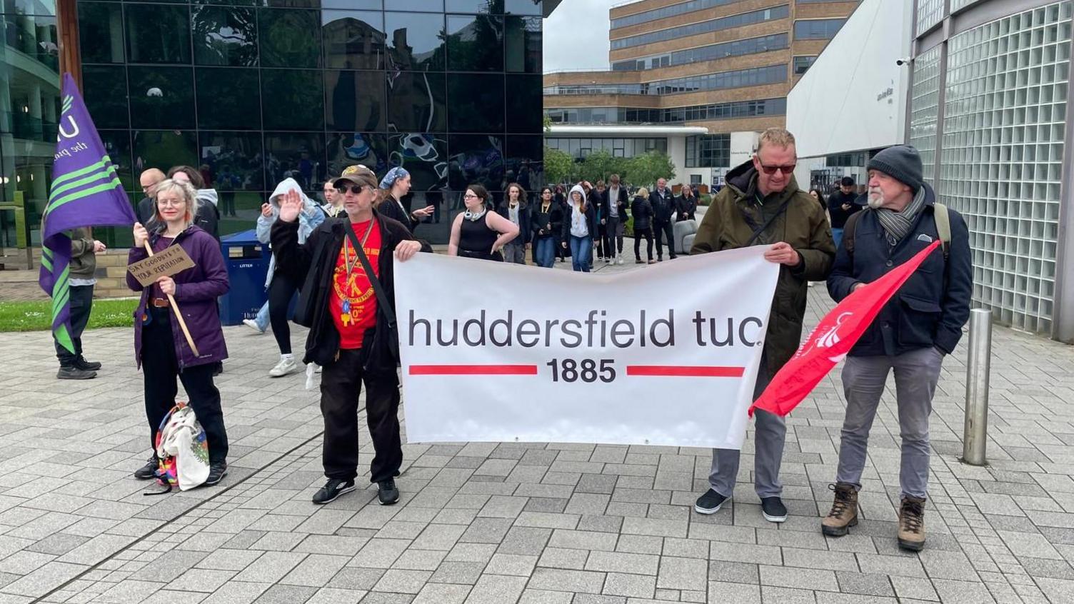 A person holding a large banner, with three people also holding flags at a protest