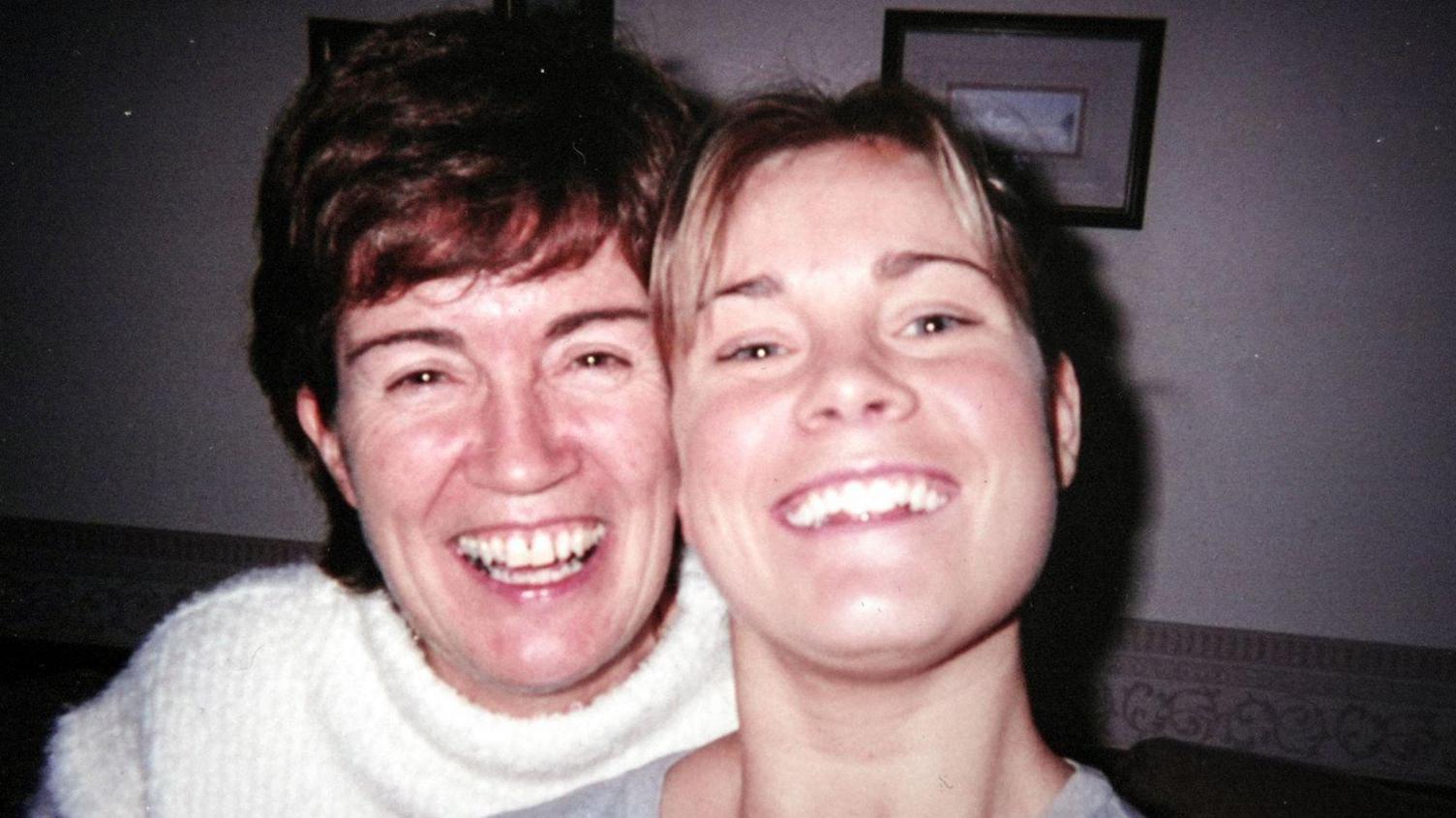 Samantha and Wendy in a picture illuminated by a flash leaving stark shadows. Samantha has short blonde hair and her mother has short reddish hair. Their faces are close together as they smile broadly for the camera.