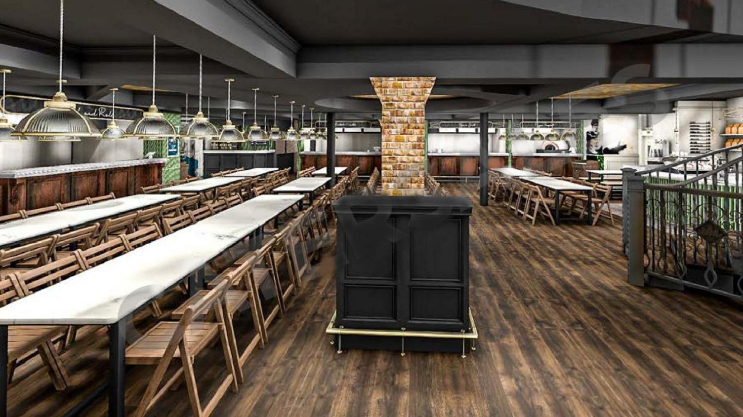 Interior of Tower Street Food Hall, Ipswich, showing long trestle tables, with rows of wooden chairs tucked in, on a wooden floor, metal and glass lights above the tables, and kitchen counters on the left and at the back.