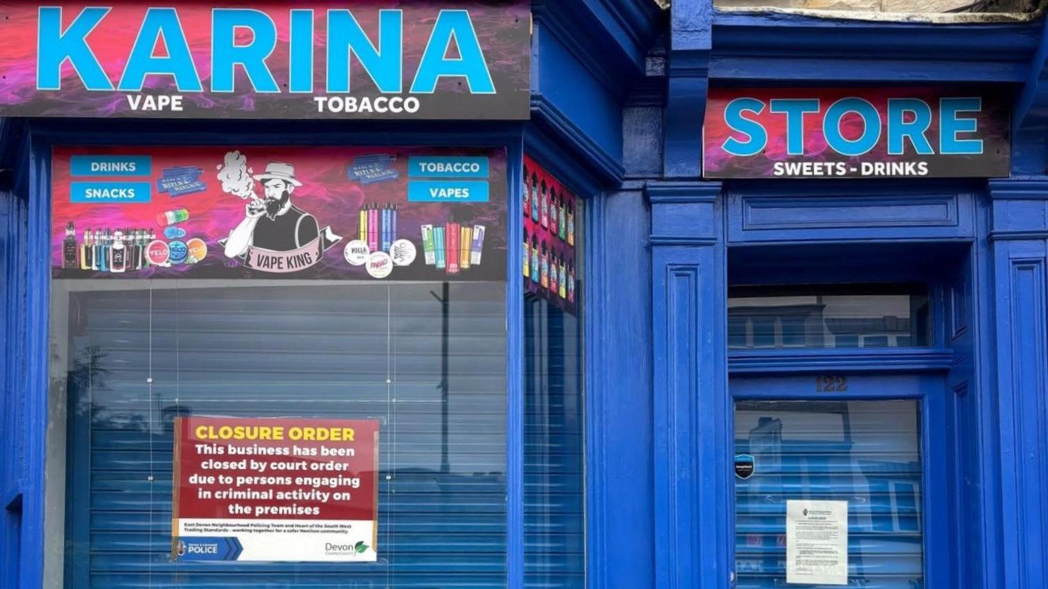 Karina Store with a closure order poster in the window. It's blue shutters are down. The outside of the shop is mainly coloured blue.
