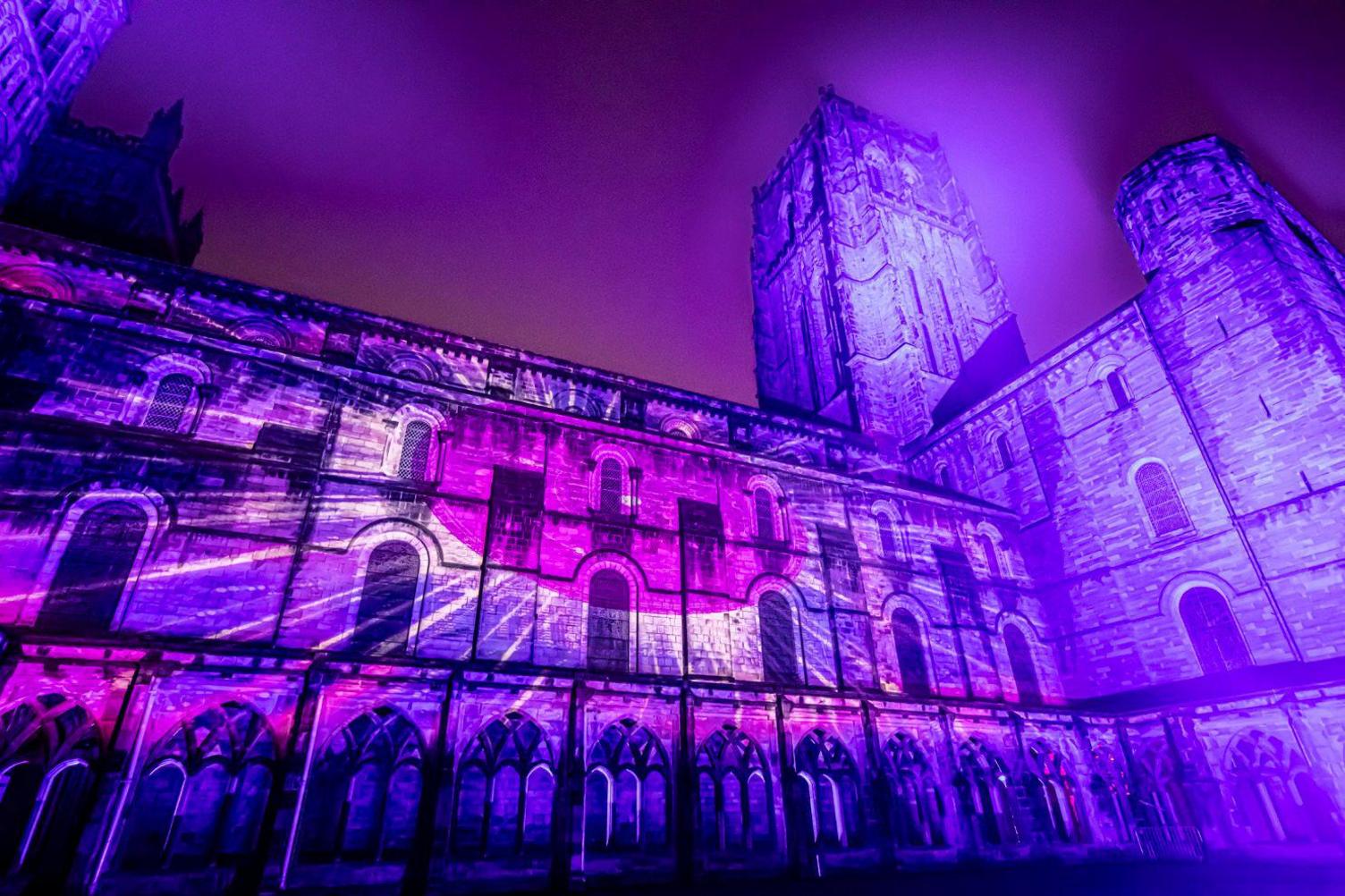 A pink sun with yellow rays is projected on the outside of the cathedral. 