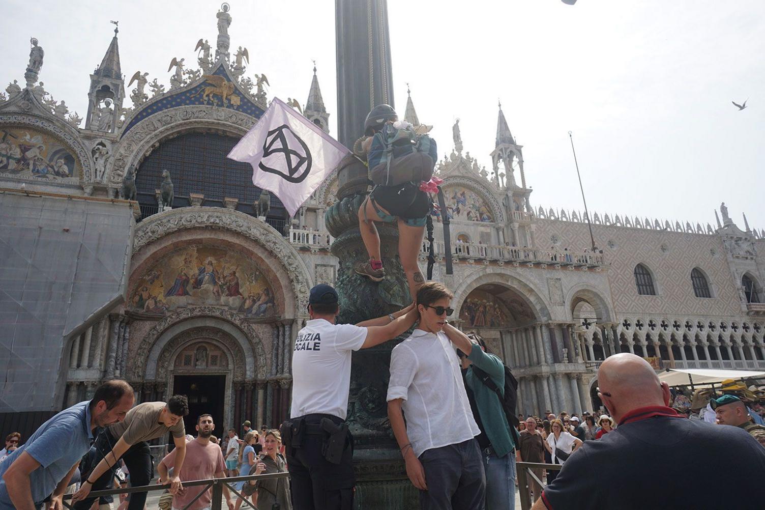 Activists protesting in Venice, Italy, against the wedding of Jeff Bezos and Lauren Sanchez. One protester carrying a flag is pictured attempting to climb a column.