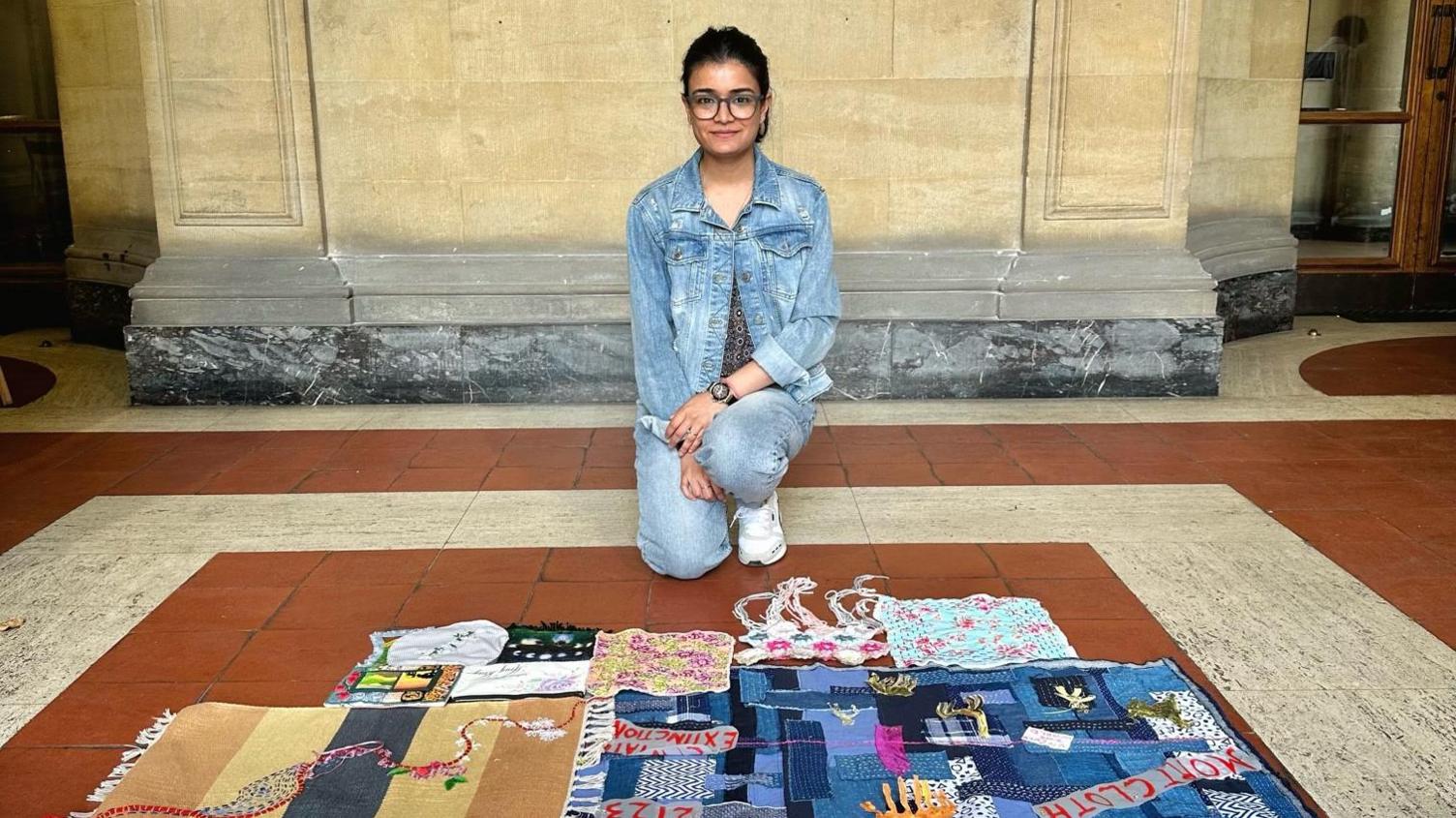 Anurita Chandola kneeling in front of a stone wall with patchwork piece on the floor in front of her